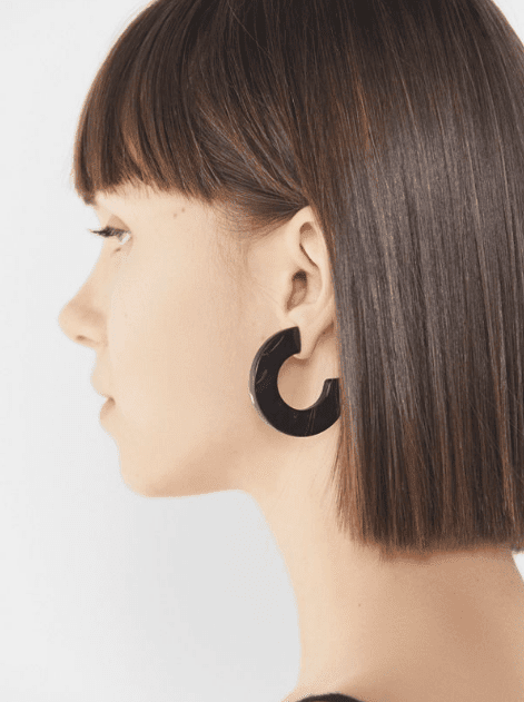 The girl with a blunt bob with massive marble earrings in deep dark color.