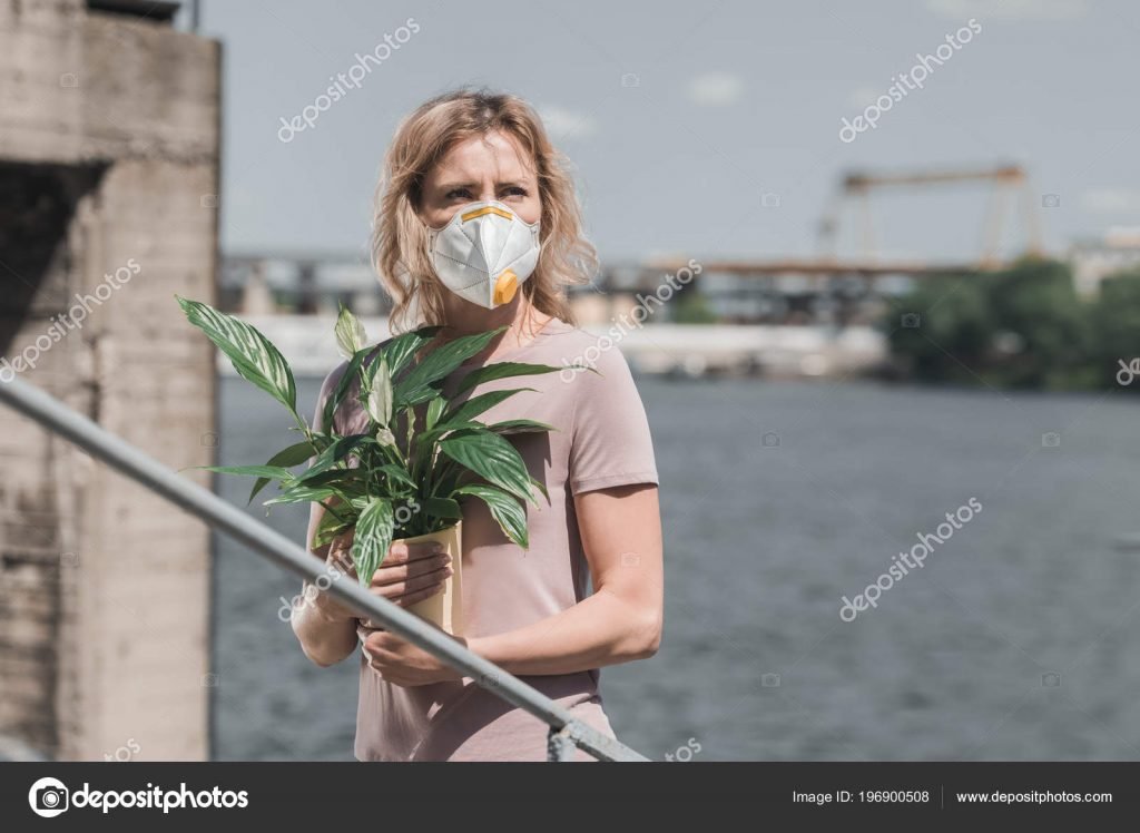 Woman in protective mask holding potted plant on bridge, air pollution concept – stock image