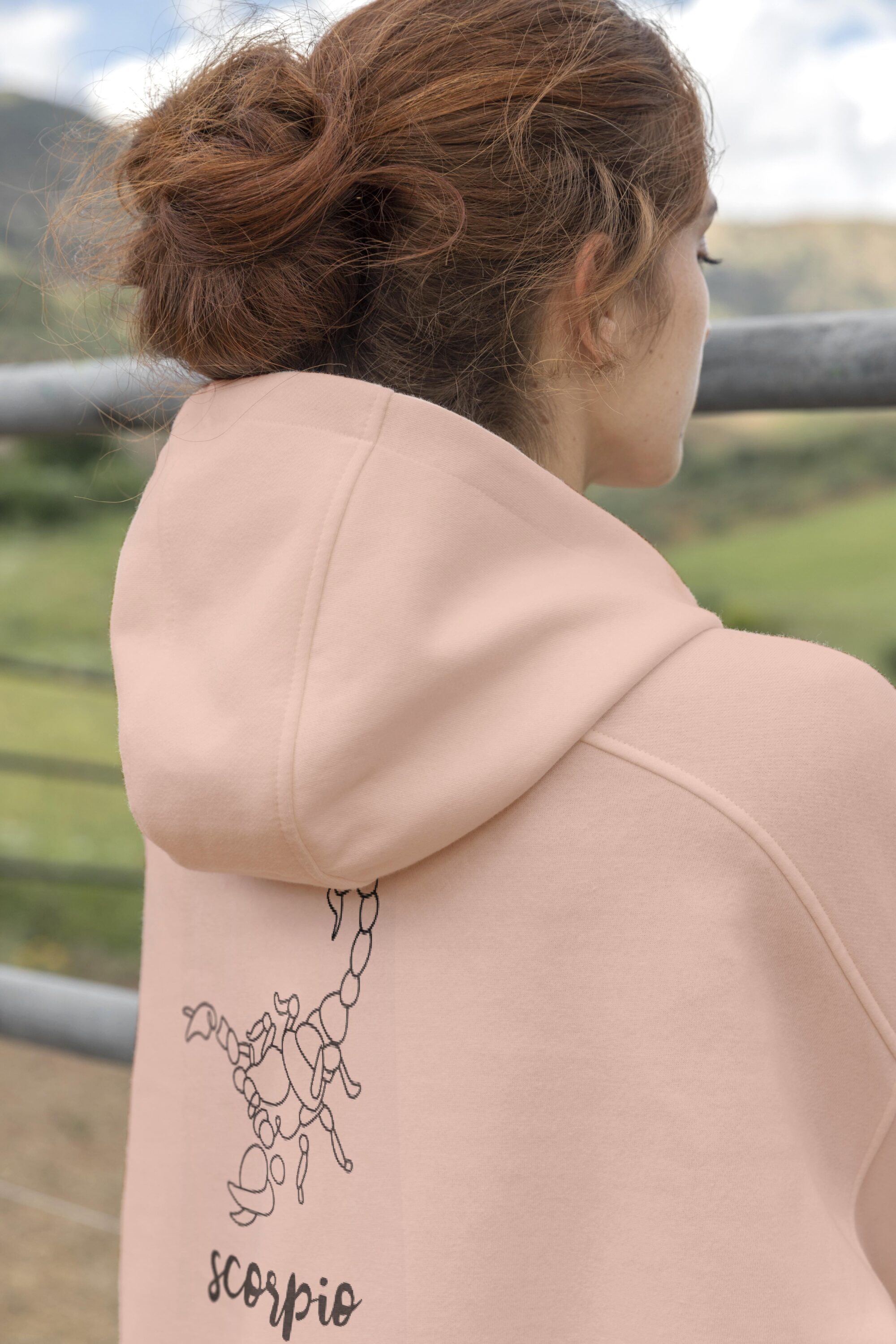 Woman in a pink hoodie looking out over a fence.
