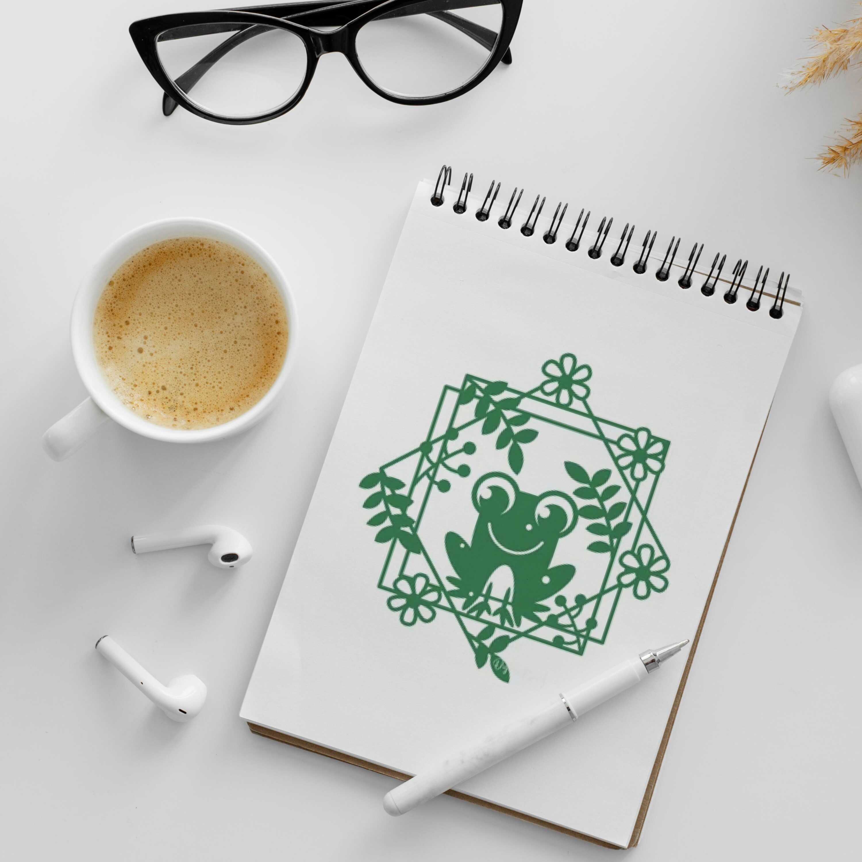 Notebook with a frog on it next to a cup of coffee.