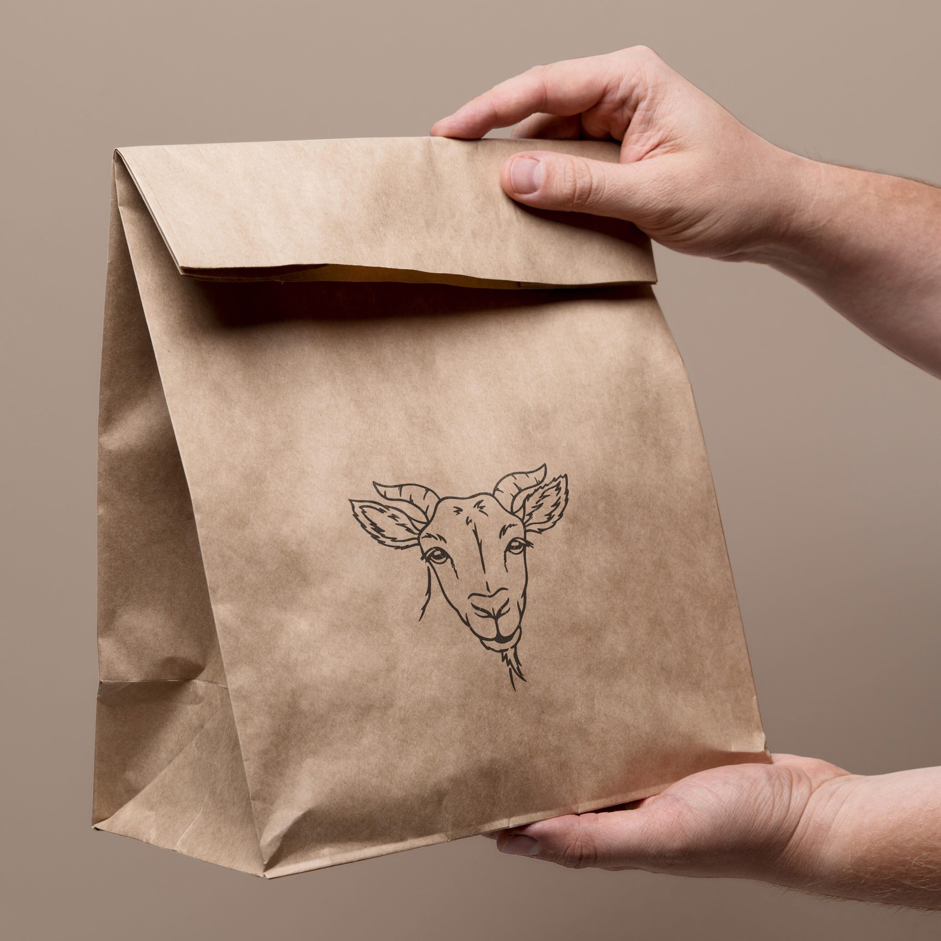 Hand holding a brown paper bag with a drawing of a deer on it.