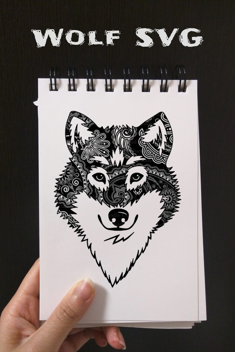 Hand holding a notebook with a drawing of a wolf.
