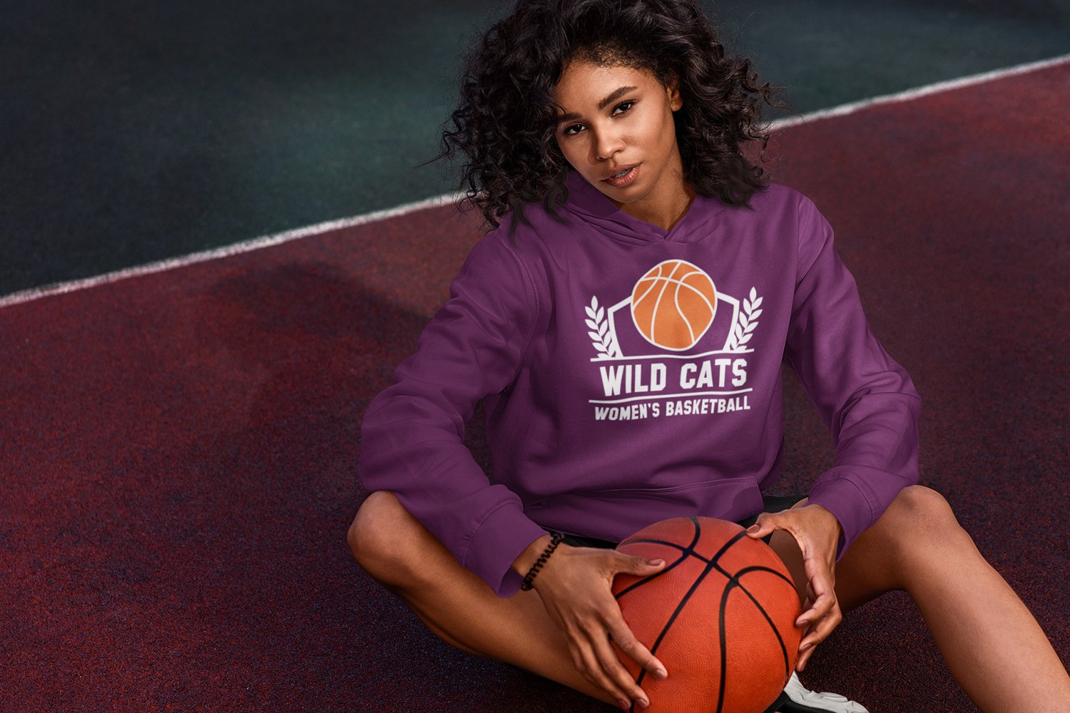 Hoodie mockup featuring a curly haired woman sitting on a basketball court.
