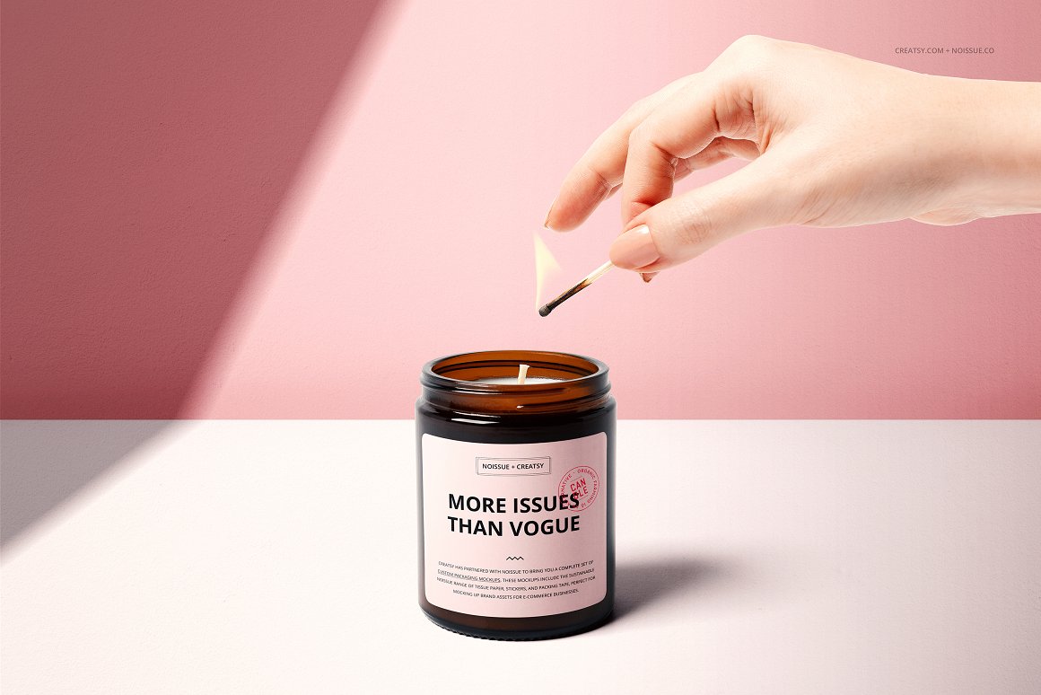 Amber glass candle with a white label and the lettering "More issues than vogue" and a woman's hand with a lit match.