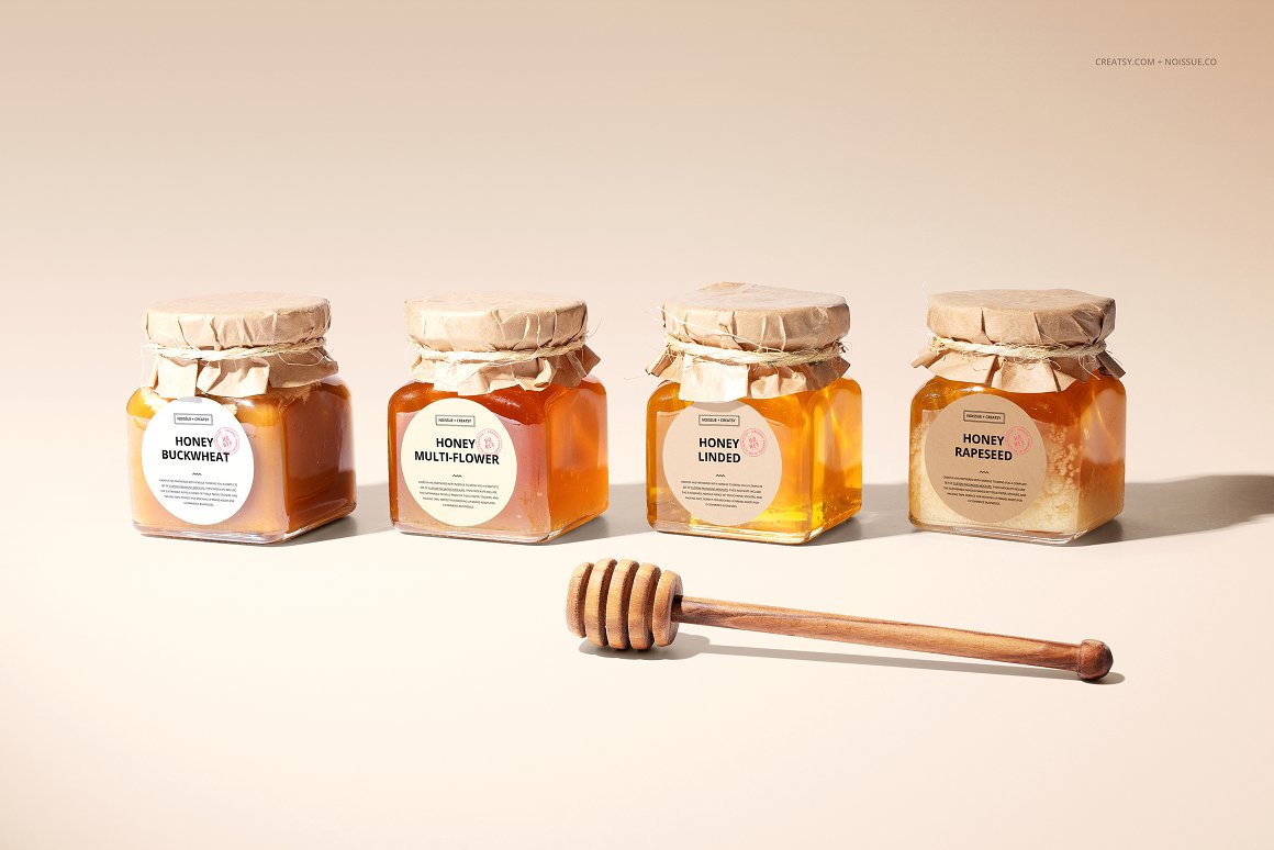4 glass jars with honey with a label with the letterings and a lid is packed in craft paper and wrapped with twine and honey spoon.