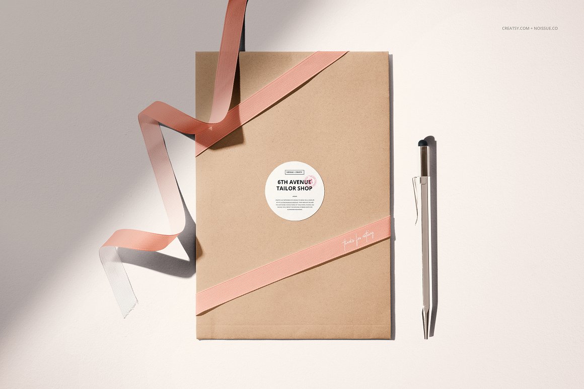Kraft bag with a white label and the inscription "6th avenue tailor shop", a pink ribbon and a black pen.