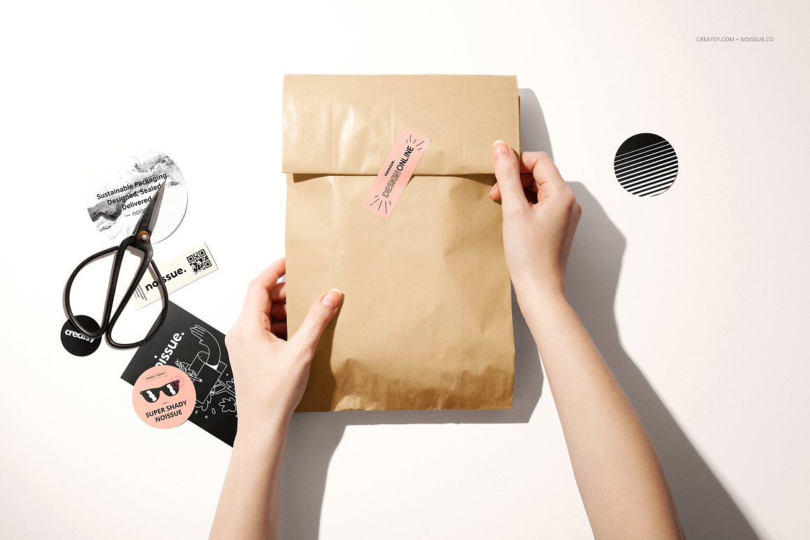 Kraft bag with a pink label and the lettering "Design online", black scissors and various black stickers.