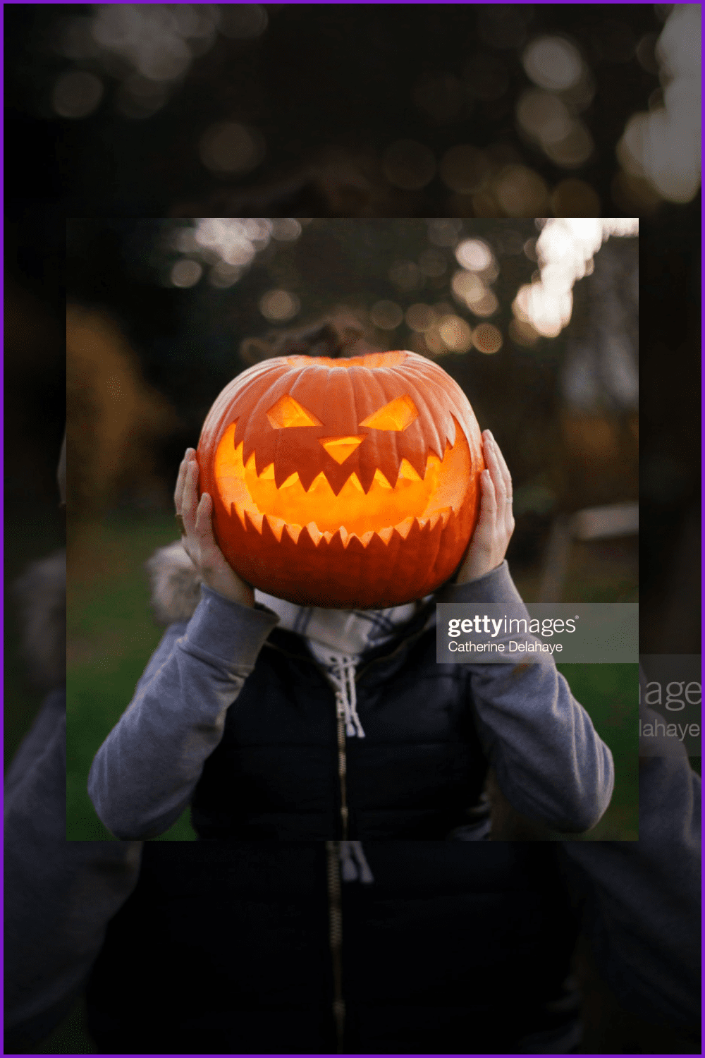A girl with halloween pumpkin in front of her head.