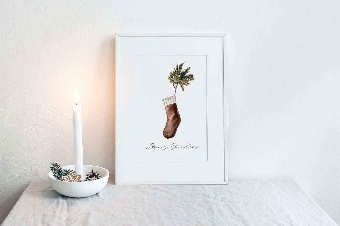Painting with a black "Merry Christmas" lettering and a brown Christmas sock on a white background in white frame.
