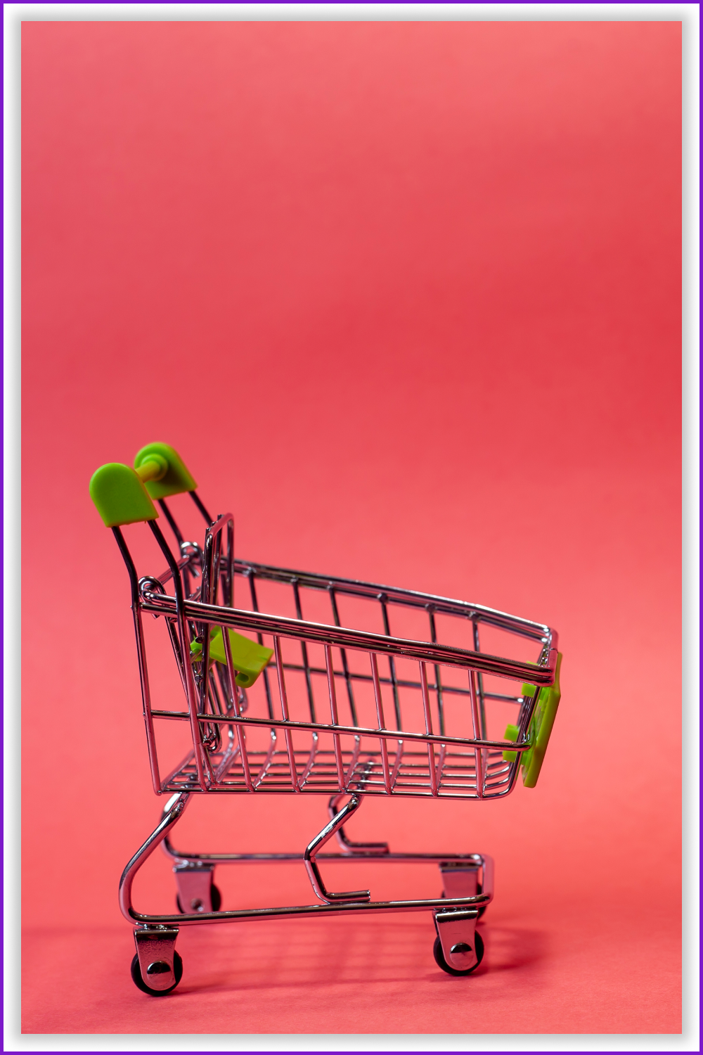 A toy little green shopping cart on a pink background.