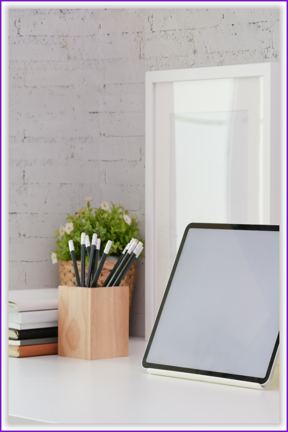 Tablet with a white screen on the table and a vase of pencils.