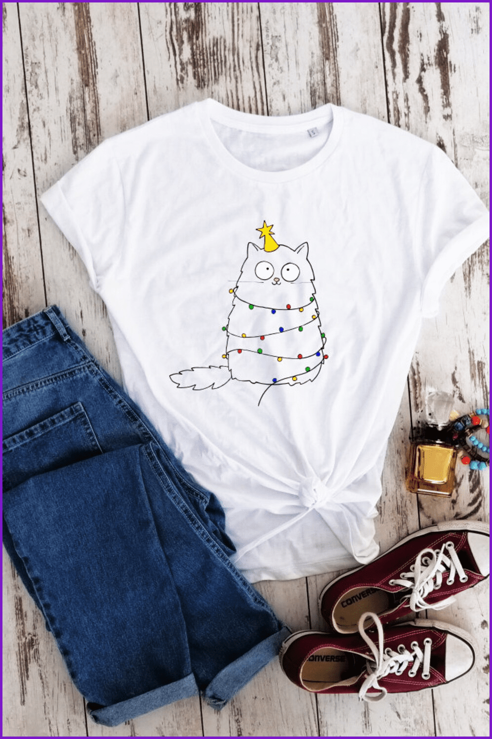 White t-shirt with a white cat with a Christmas tree star on its head and lights hanging over its body.