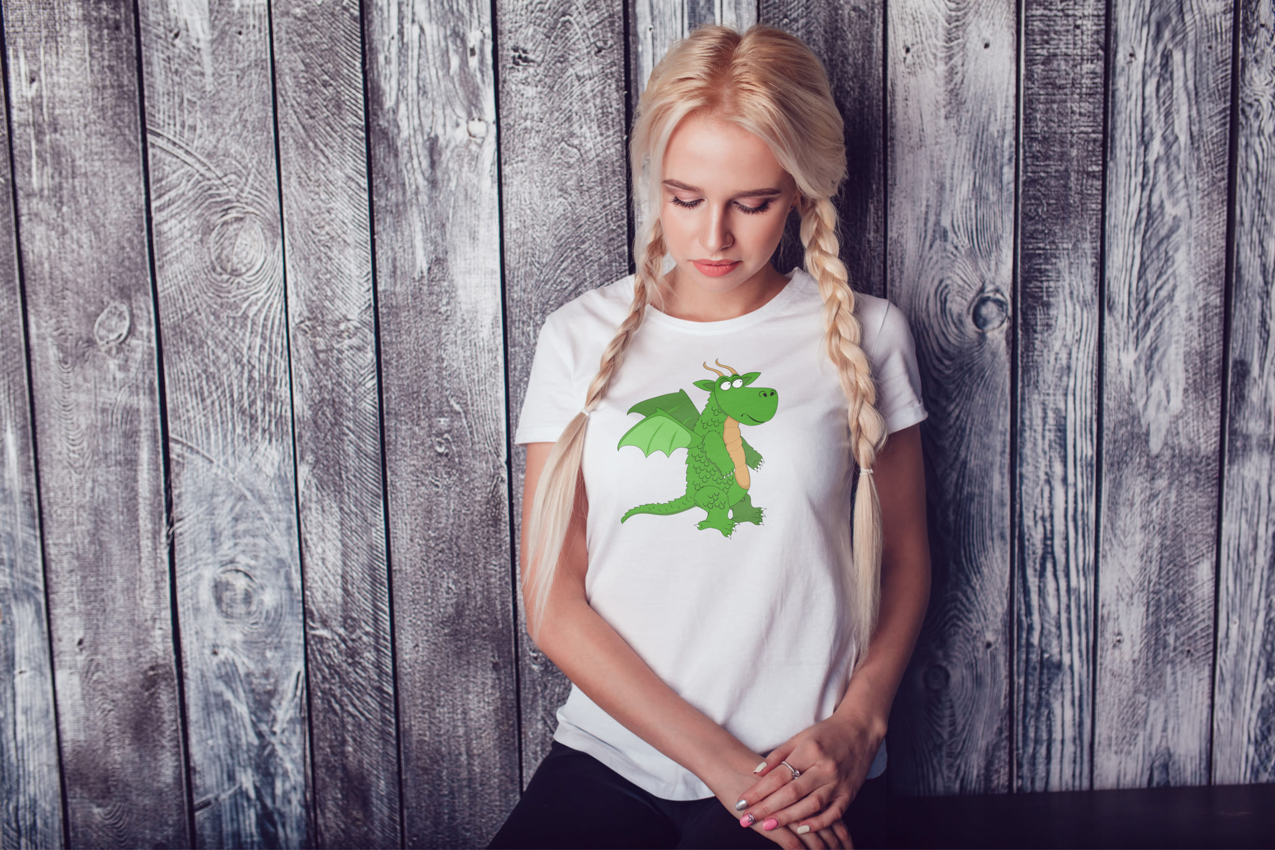 A girl with blond hair and a white T-shirt with a light green dragon.