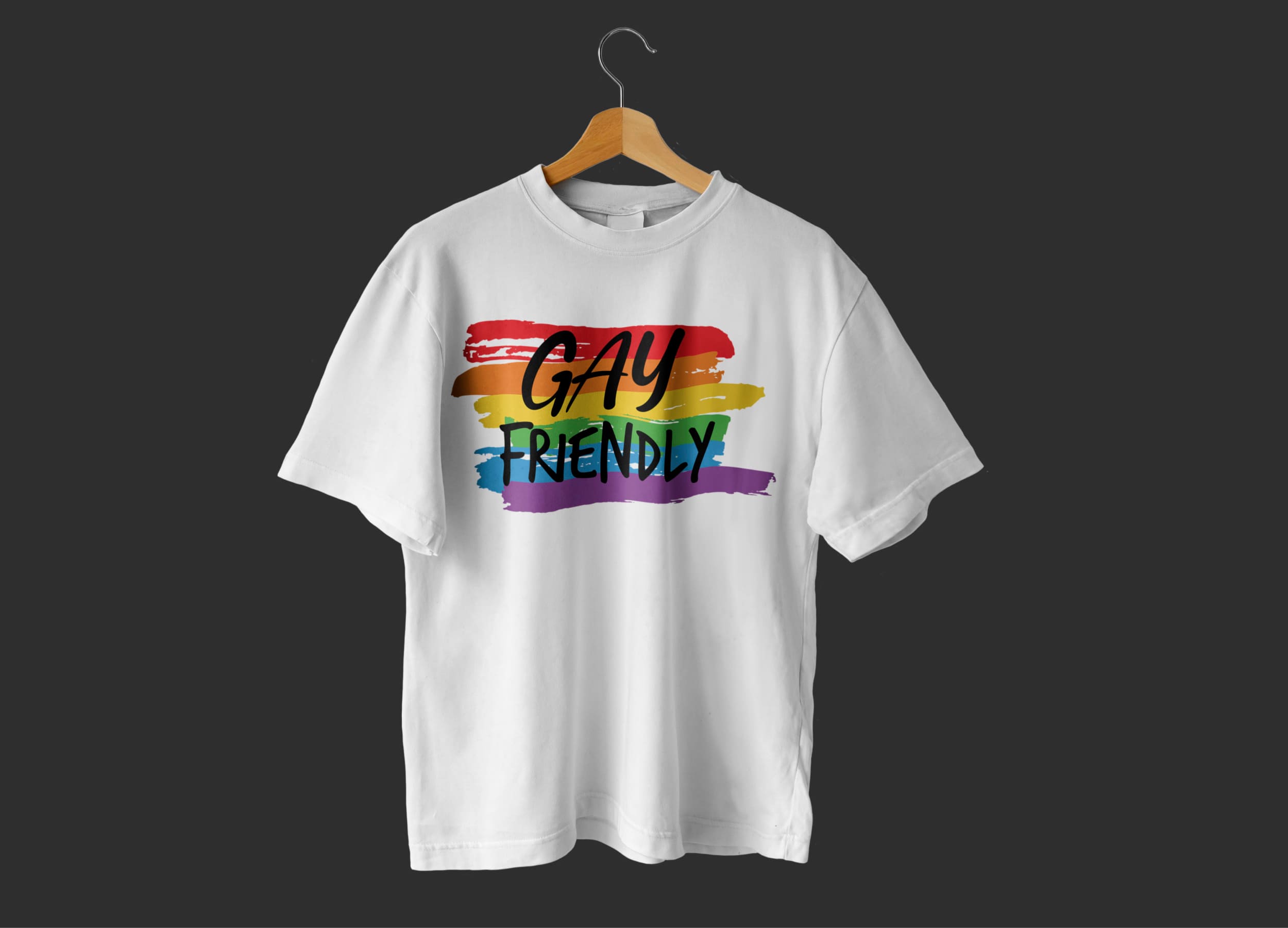 A white t-shirt with the black lettering "Be proud" against an LGBT flag on a hanger and on a dark gray background.
