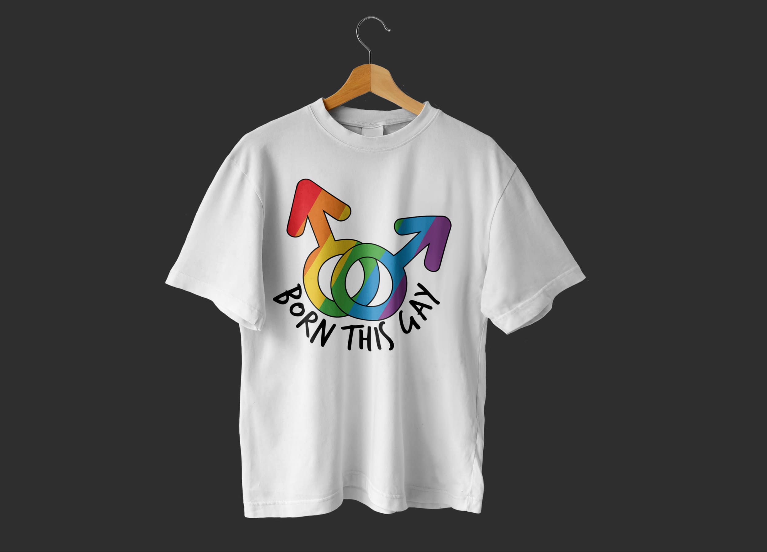A white t-shirt with two male gender symbols in the colors of the LGBT flag and the black lettering "Born this gay" on a hanger and on a dark gray background.