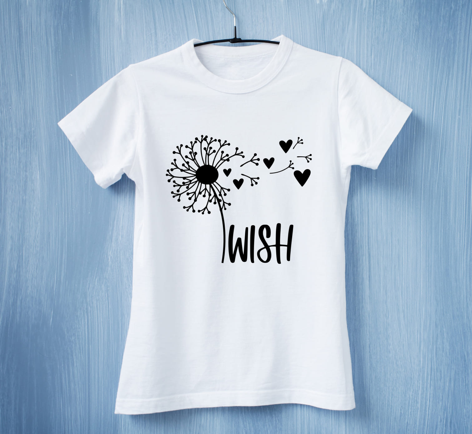 A white t-shirt with a black dandelion flower with black hearts and black kettering "WIsh" on a blue background.