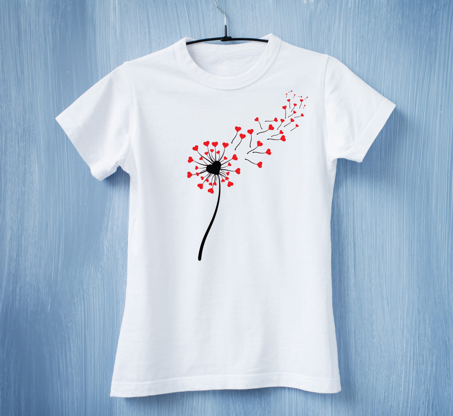 A white t-shirt with a black dandelion flower with red hearts on a blue background.