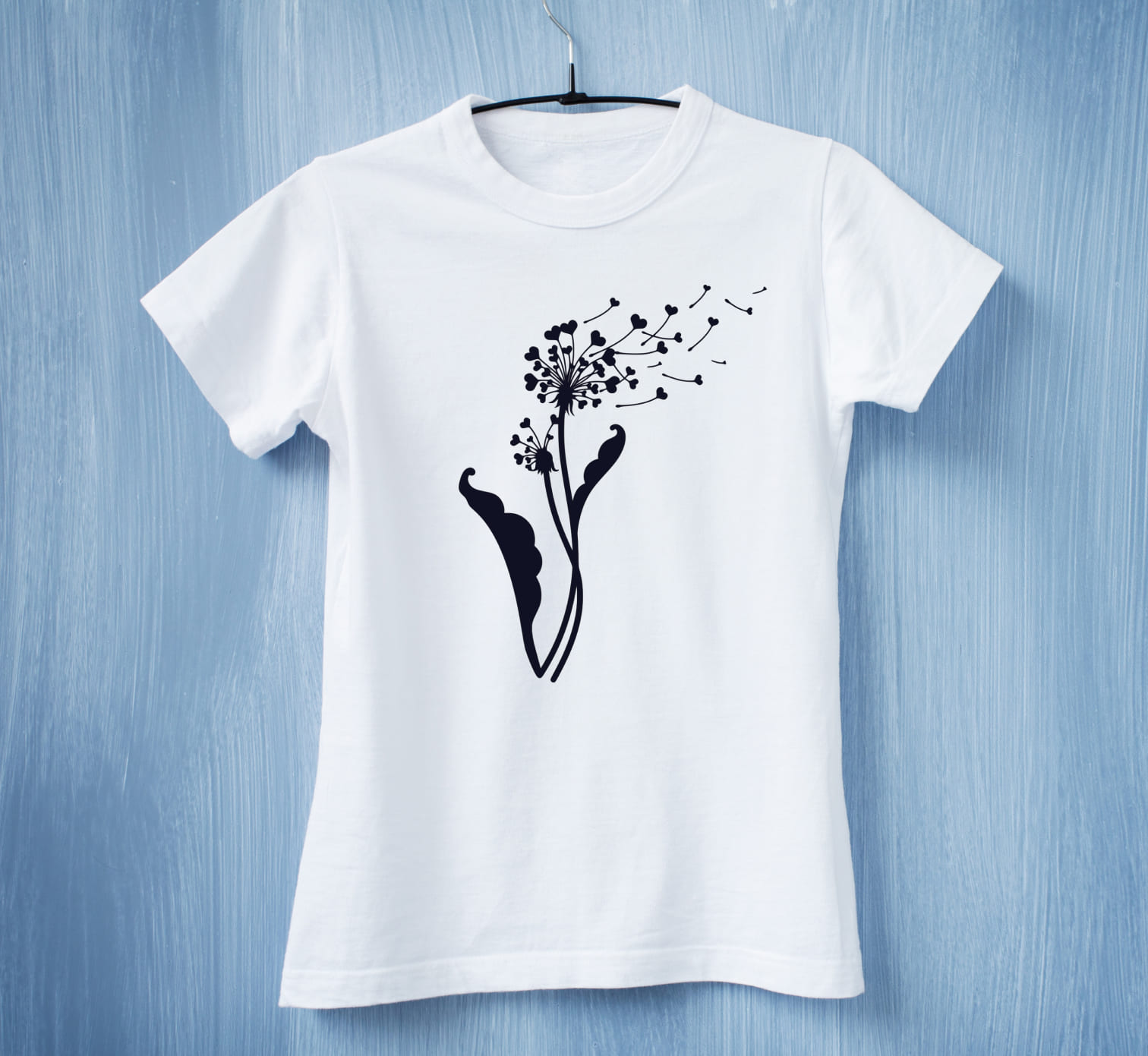A white t-shirt with a black dandelion flower with black hearts on a blue background.