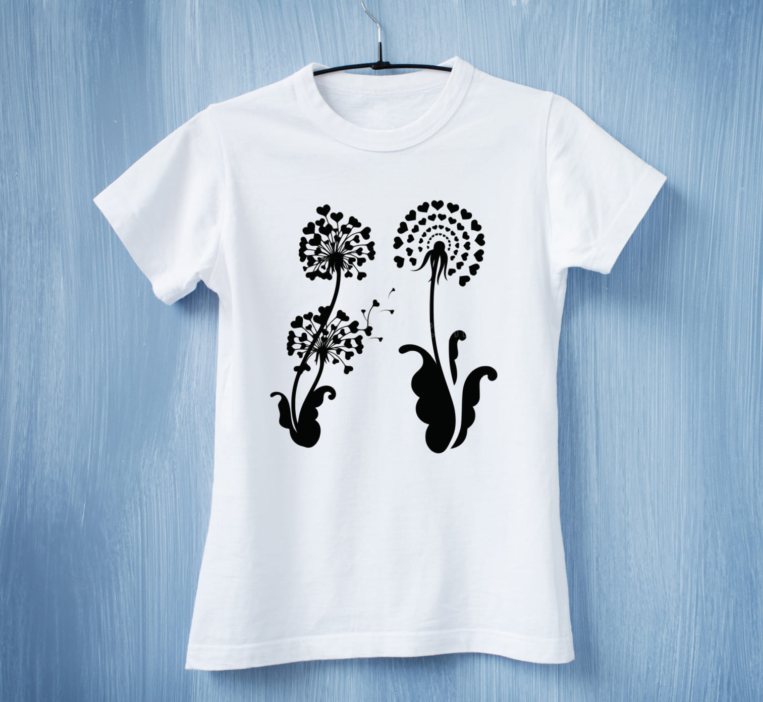 A white t-shirt with 2 black dandelion flowers with black hearts on a blue background.