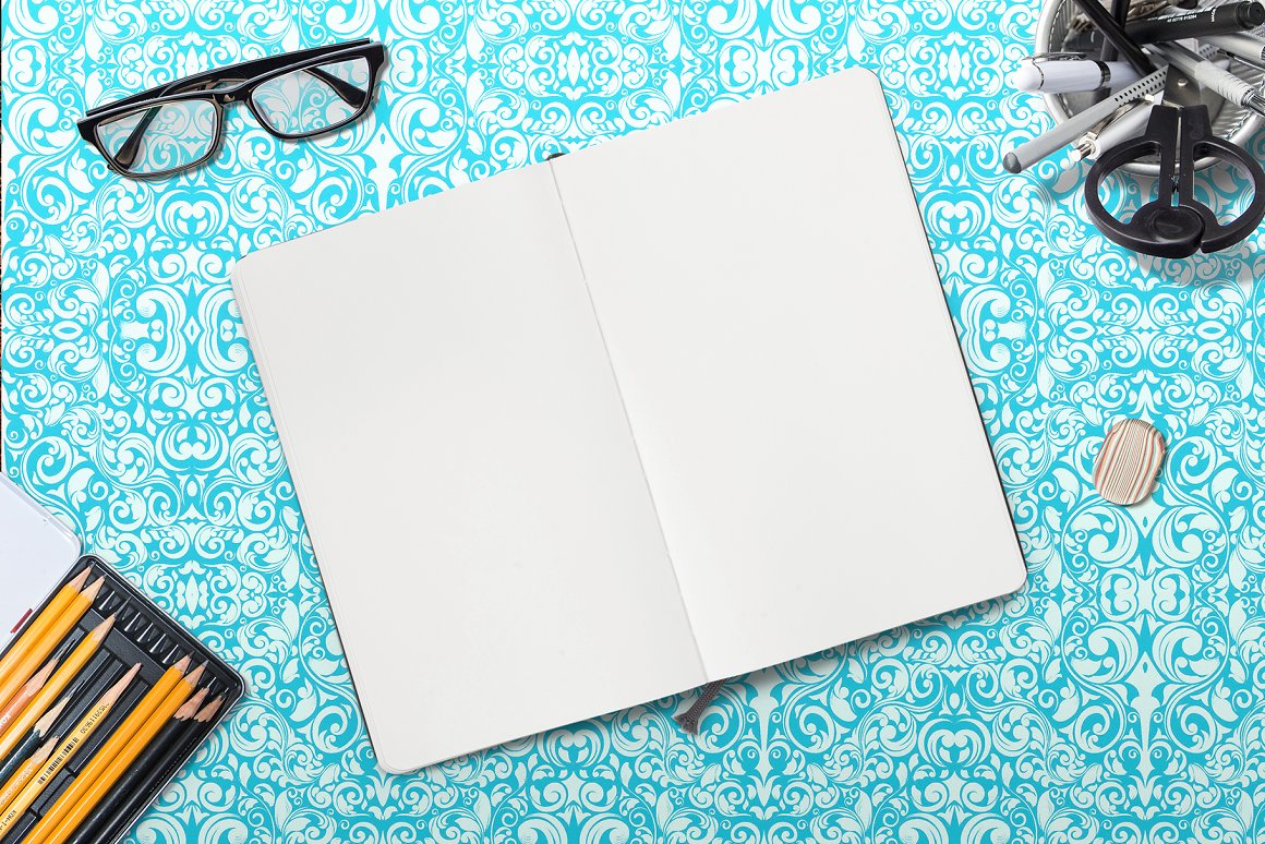Mockup of a lying notebook in open view and different stationery on light blue abstract background.