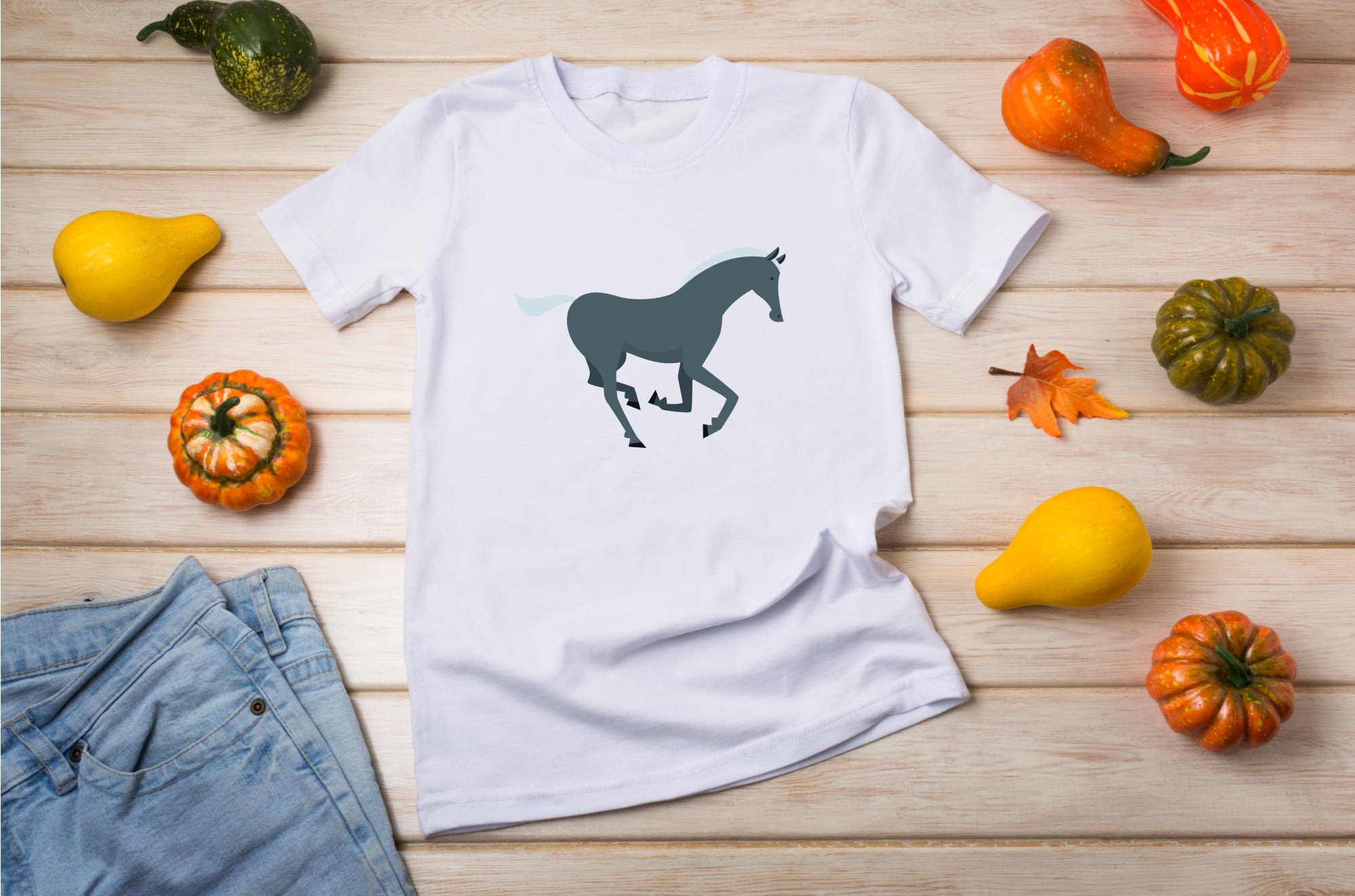 White t-shirt with a dark gray mustang horse on the wooden background with pumpkins.