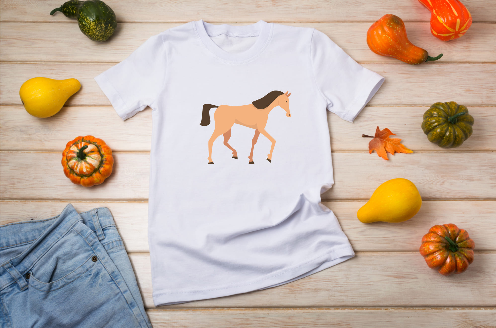 White t-shirt with a beige mustang horse on the wooden background with pumpkins.