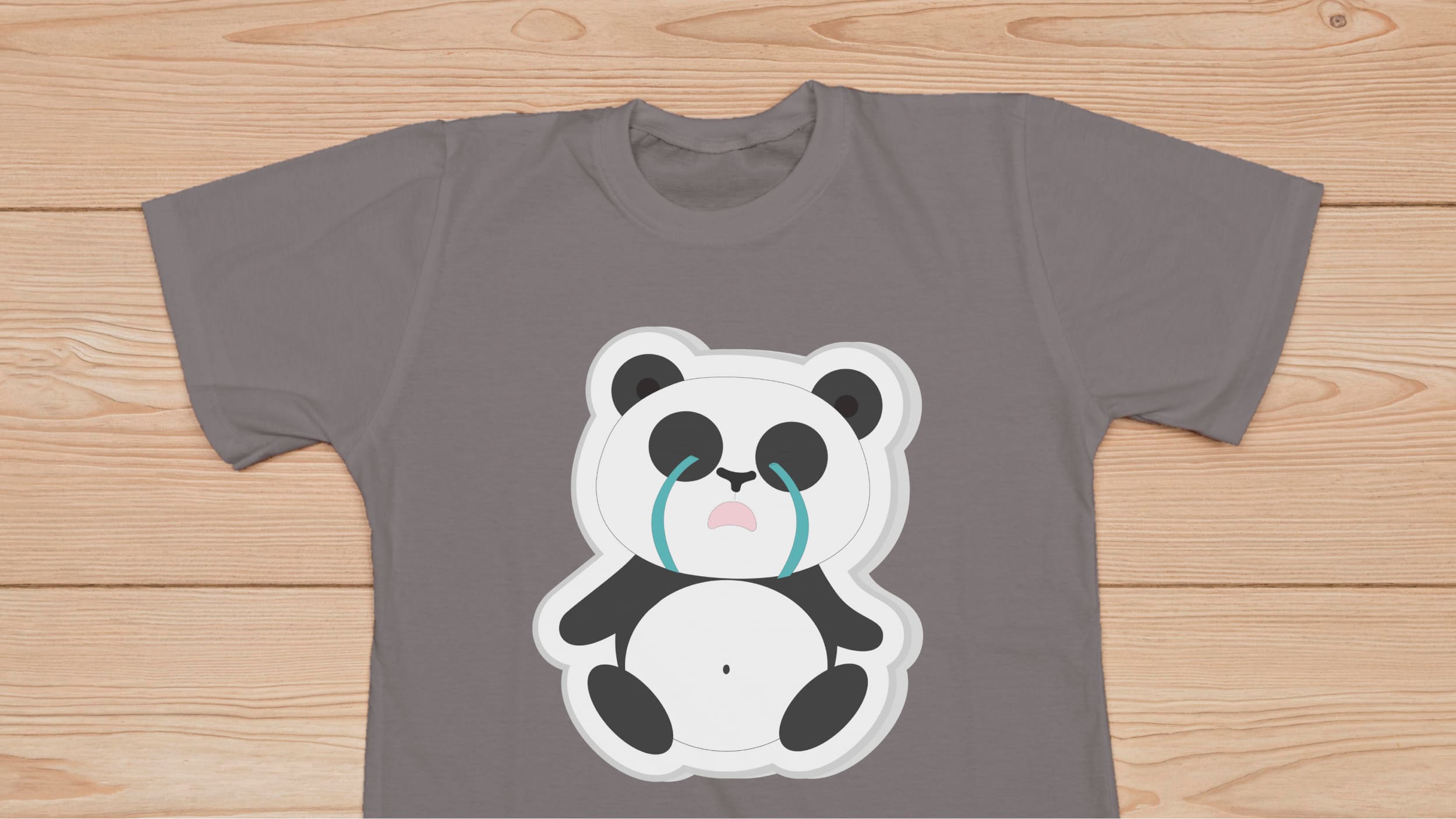 Gray t-shirt with a tearful panda bear on a wooden background.