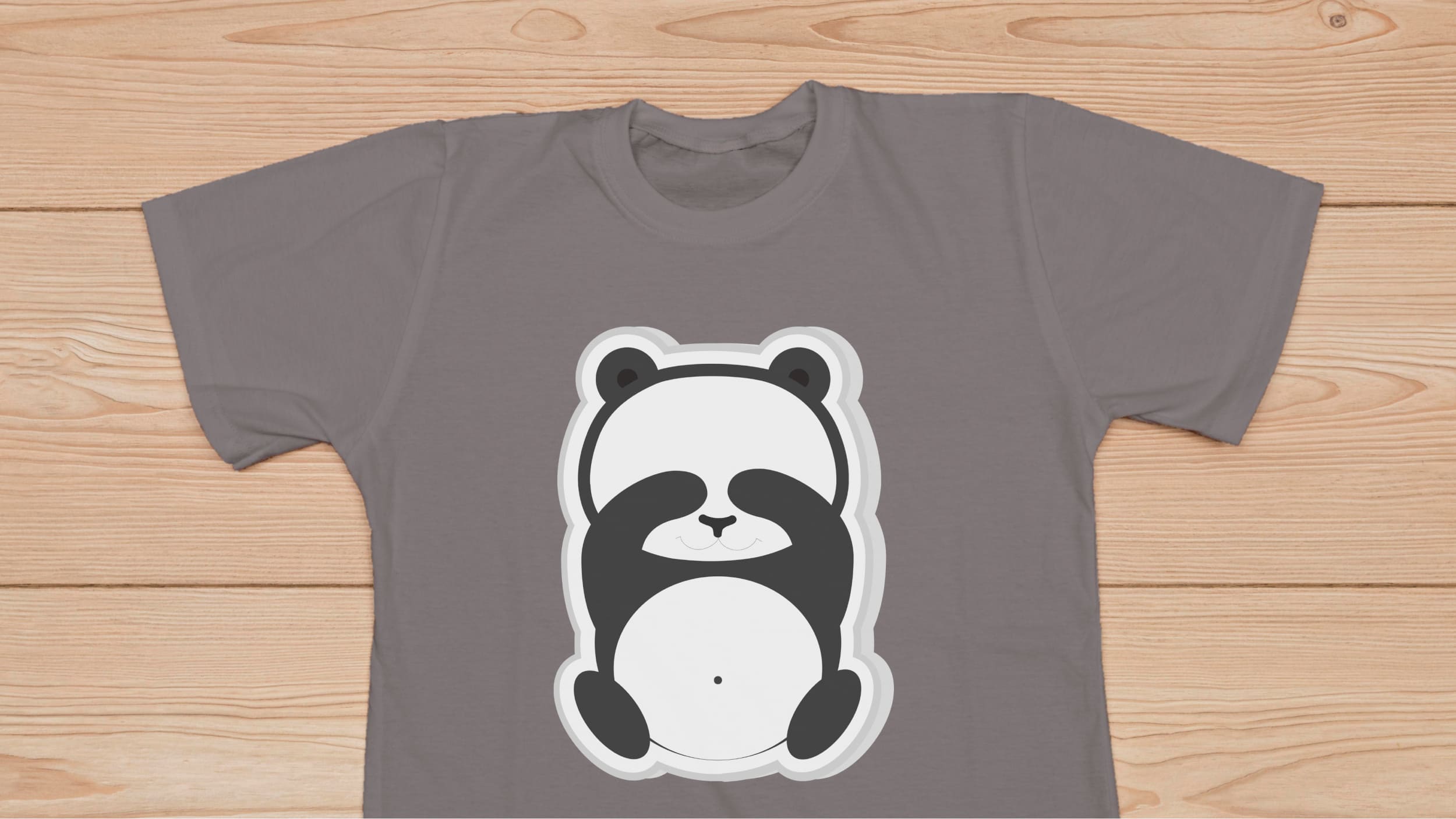 Gray t-shirt with a sad panda bear on a wooden background.