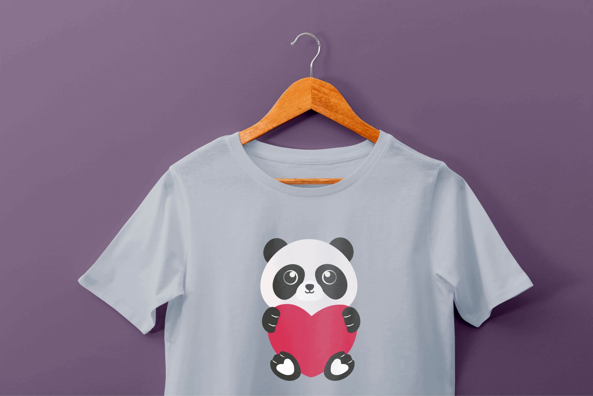 Light blue t-shirt with a panda and pink heart on a hanger on a purple background.
