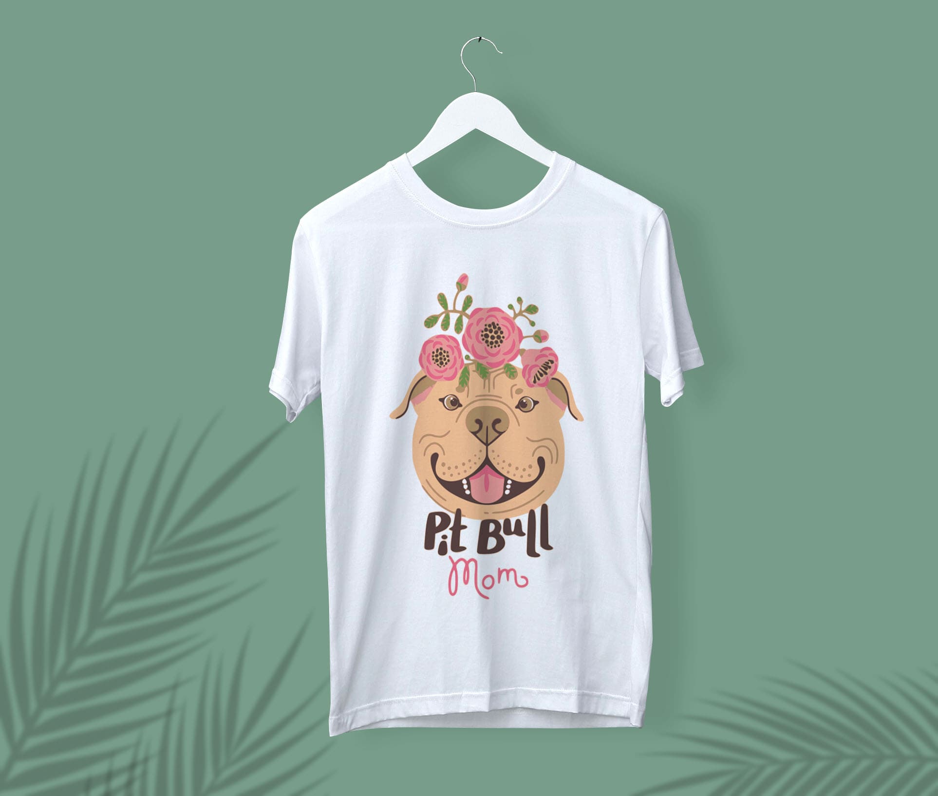 White t-shirt with a pitbull mom face and flowers on a white hanger, on a green background.