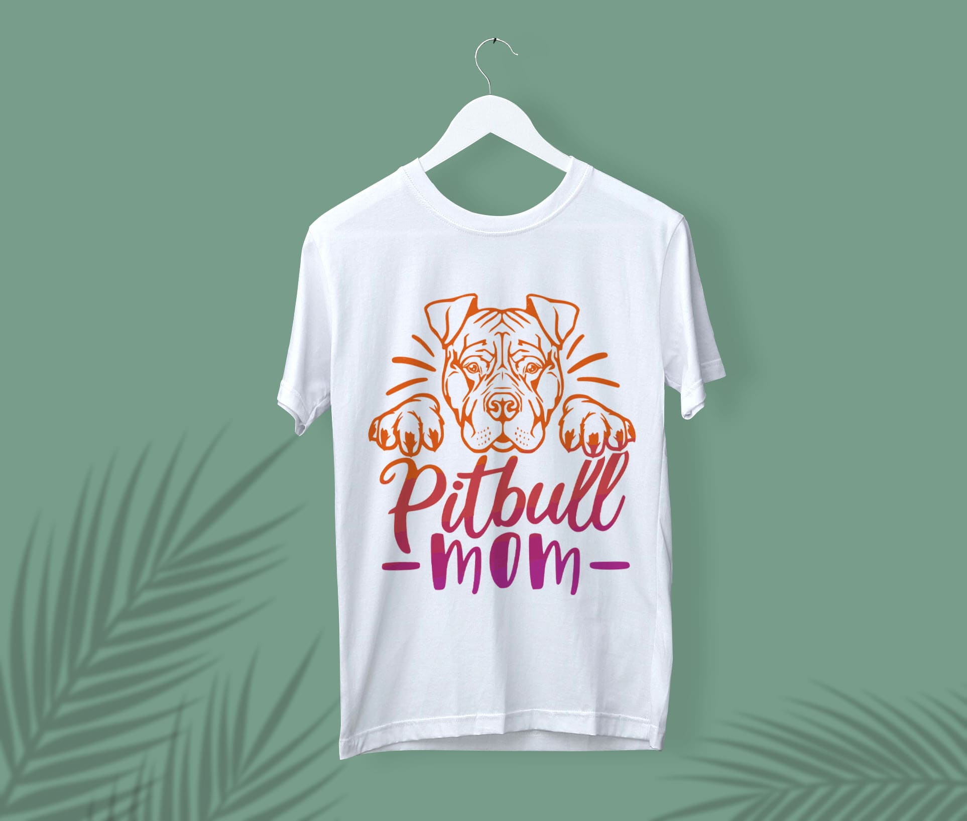 White t-shirt with an orange and pink pitbull mom face on a white hanger, on a green background.