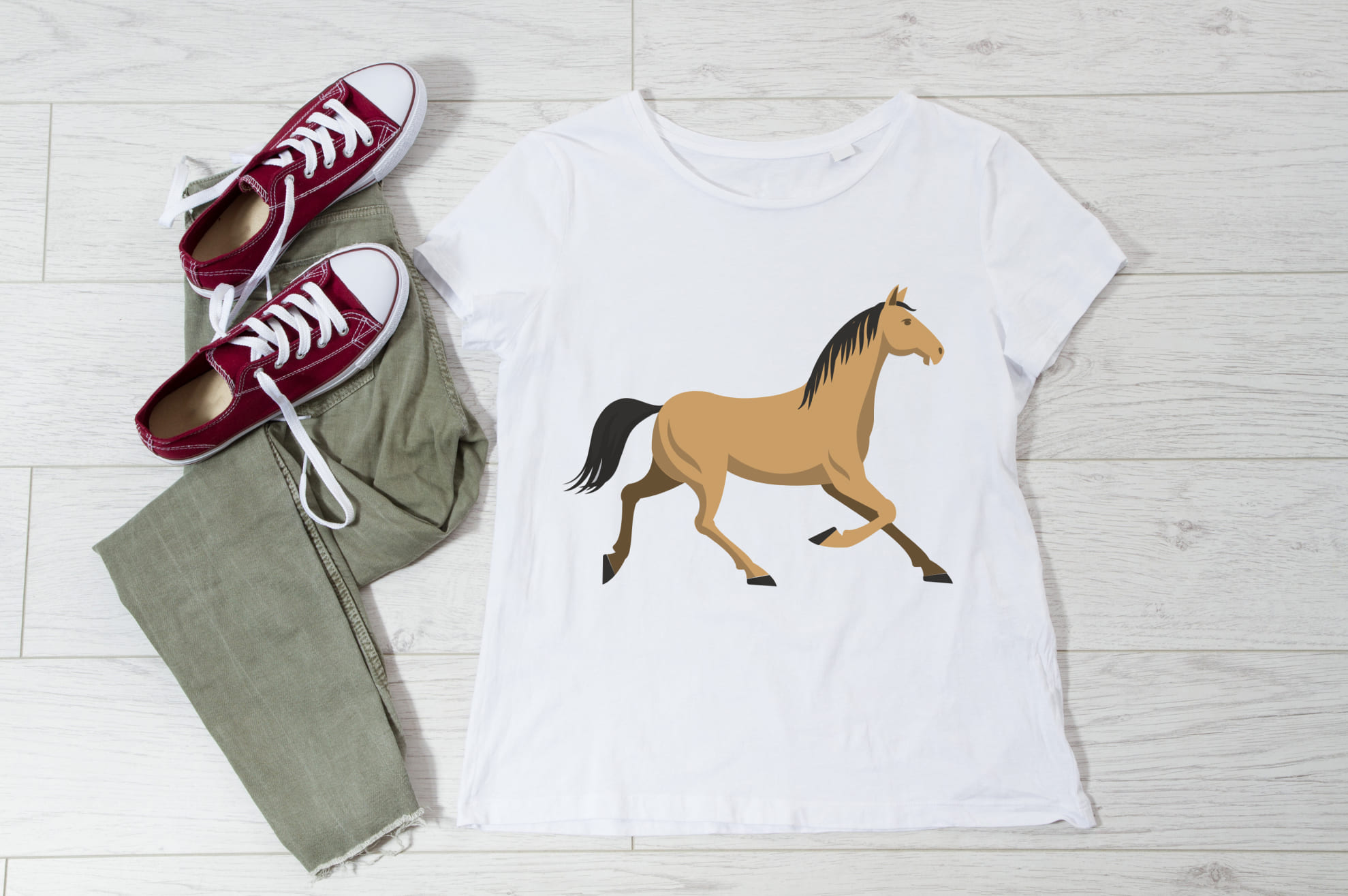 White t-shirt with an image of a horse, and sneakers with trousers on the wooden background.