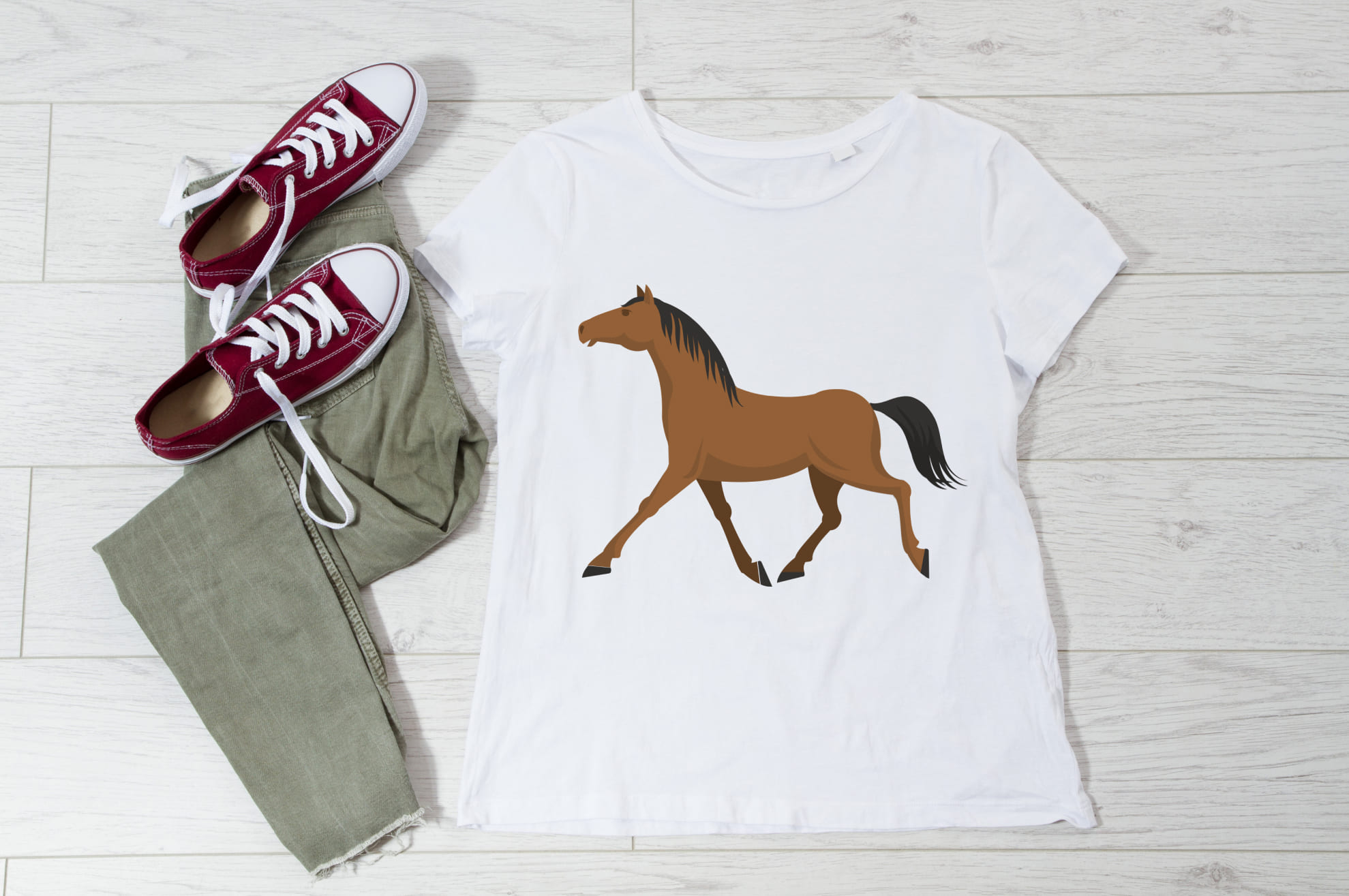 White t-shirt with an image of a brown horse, and sneakers with trousers on the wooden background.