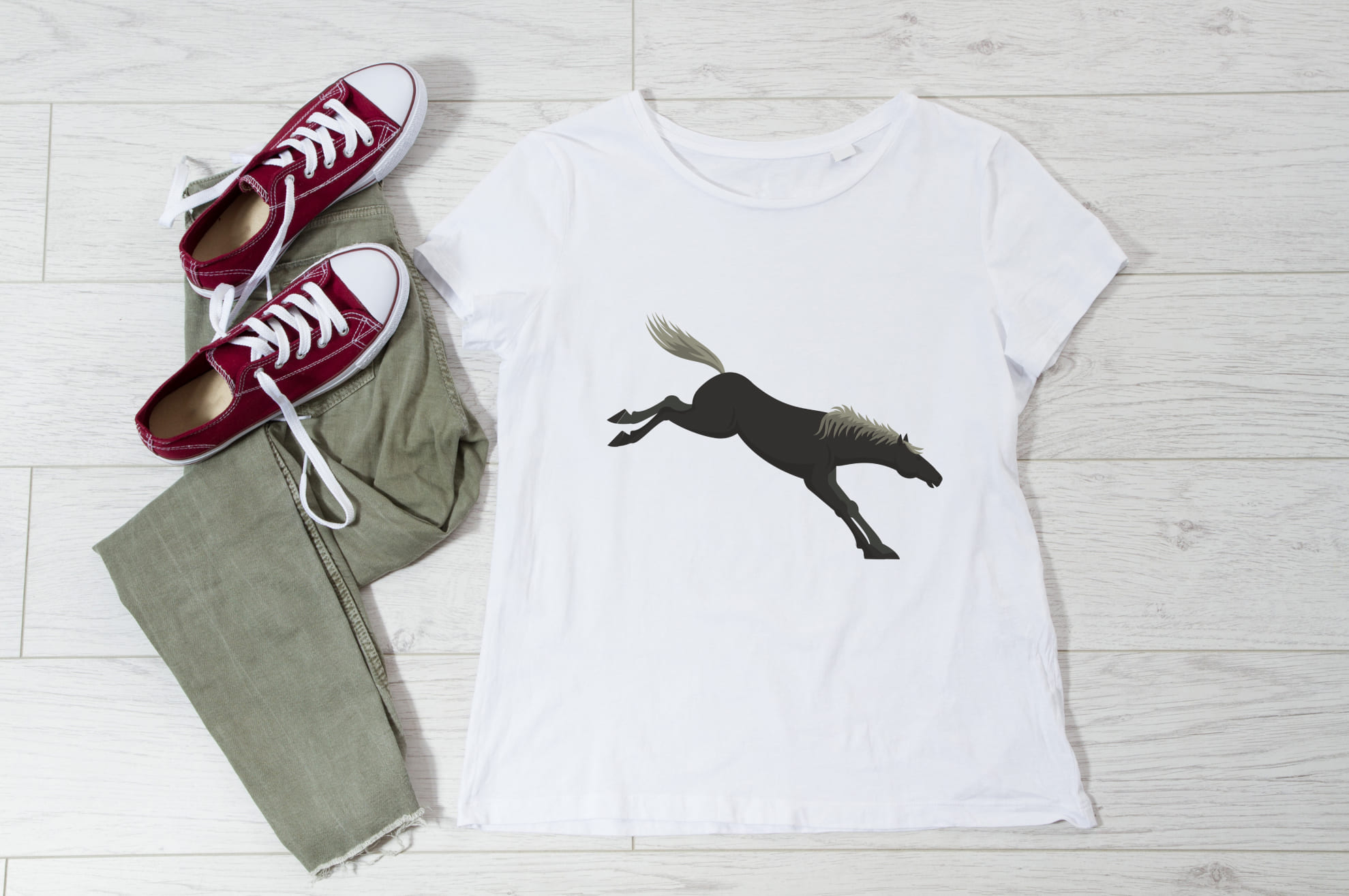 White t-shirt with an image of a black horse, and sneakers with trousers on the wooden background.