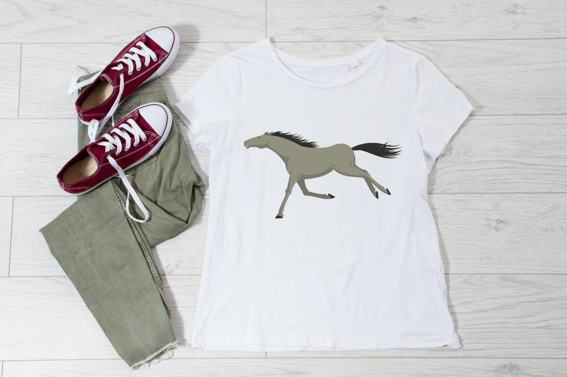 White t-shirt with an image of a gray horse, and sneakers with trousers on the wooden background.