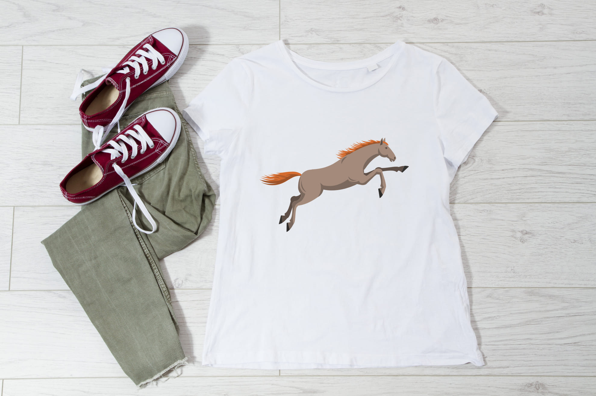 White t-shirt with an image of a running horse, and sneakers with trousers on the wooden background.