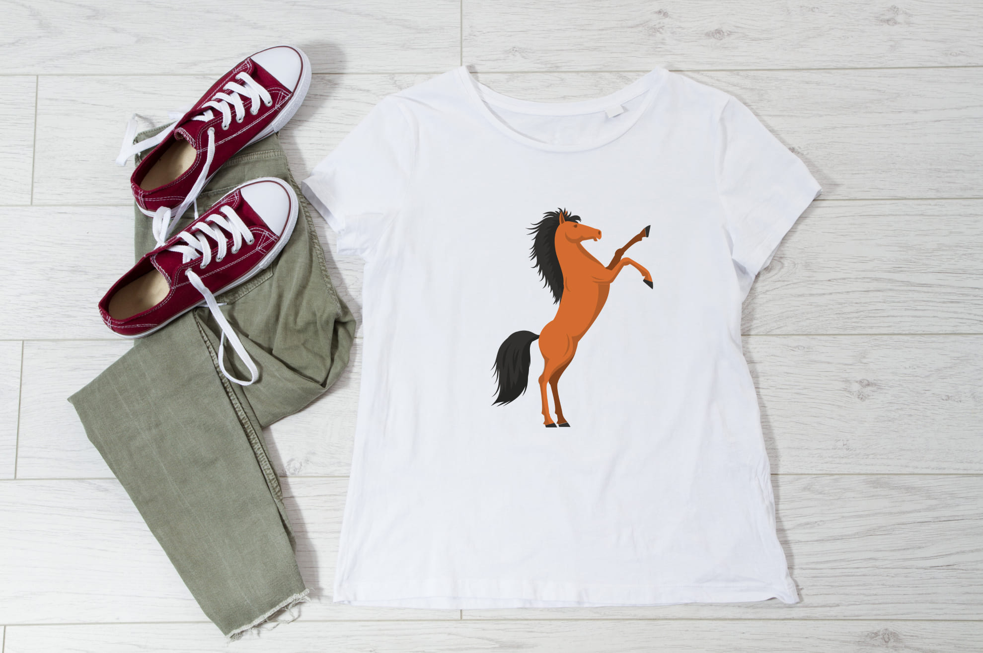 White t-shirt with an image of a ginger horse, and sneakers with trousers on the wooden background.