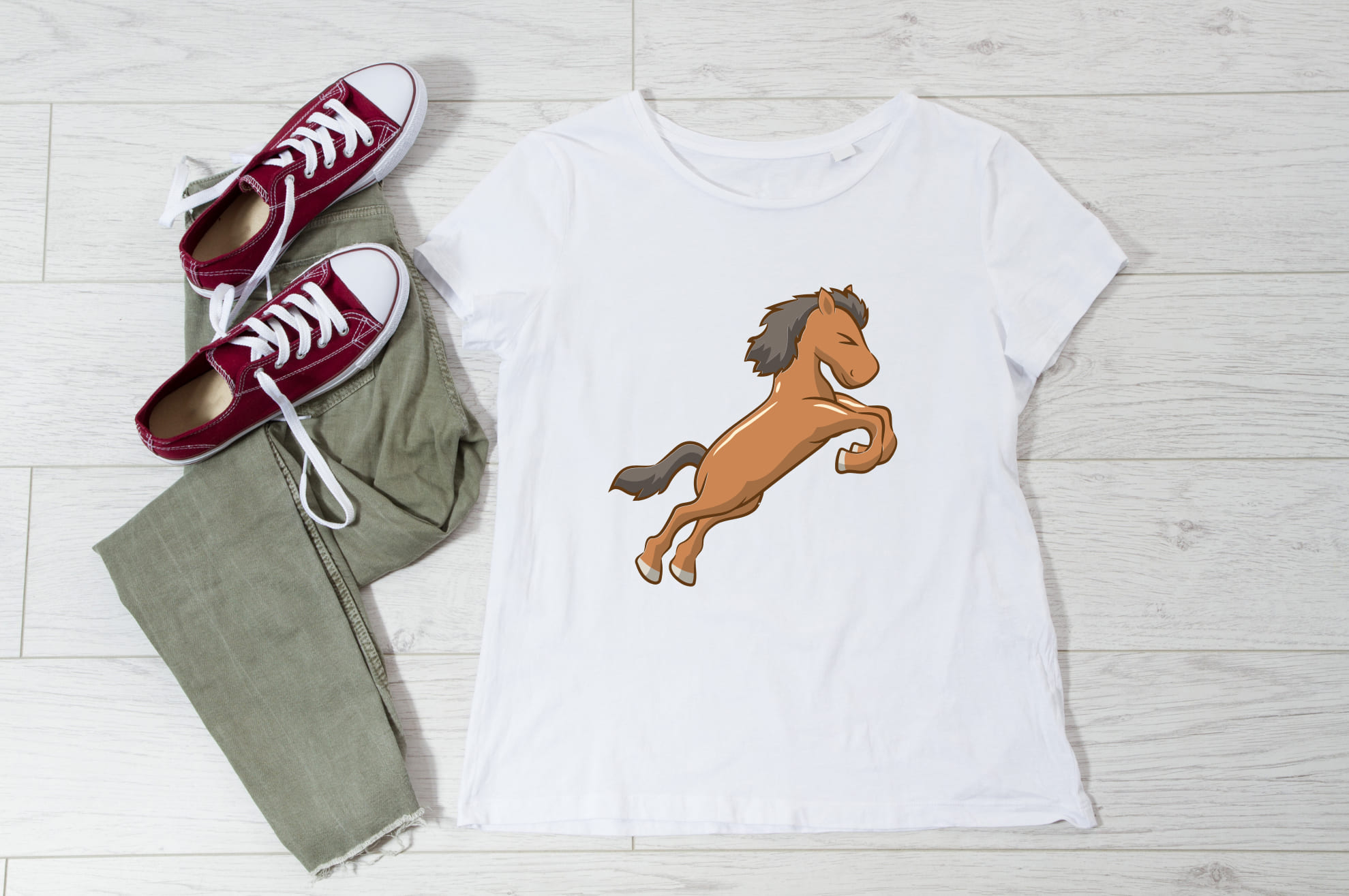 White t-shirt with an image of a baby horse, and sneakers with trousers on the wooden background.