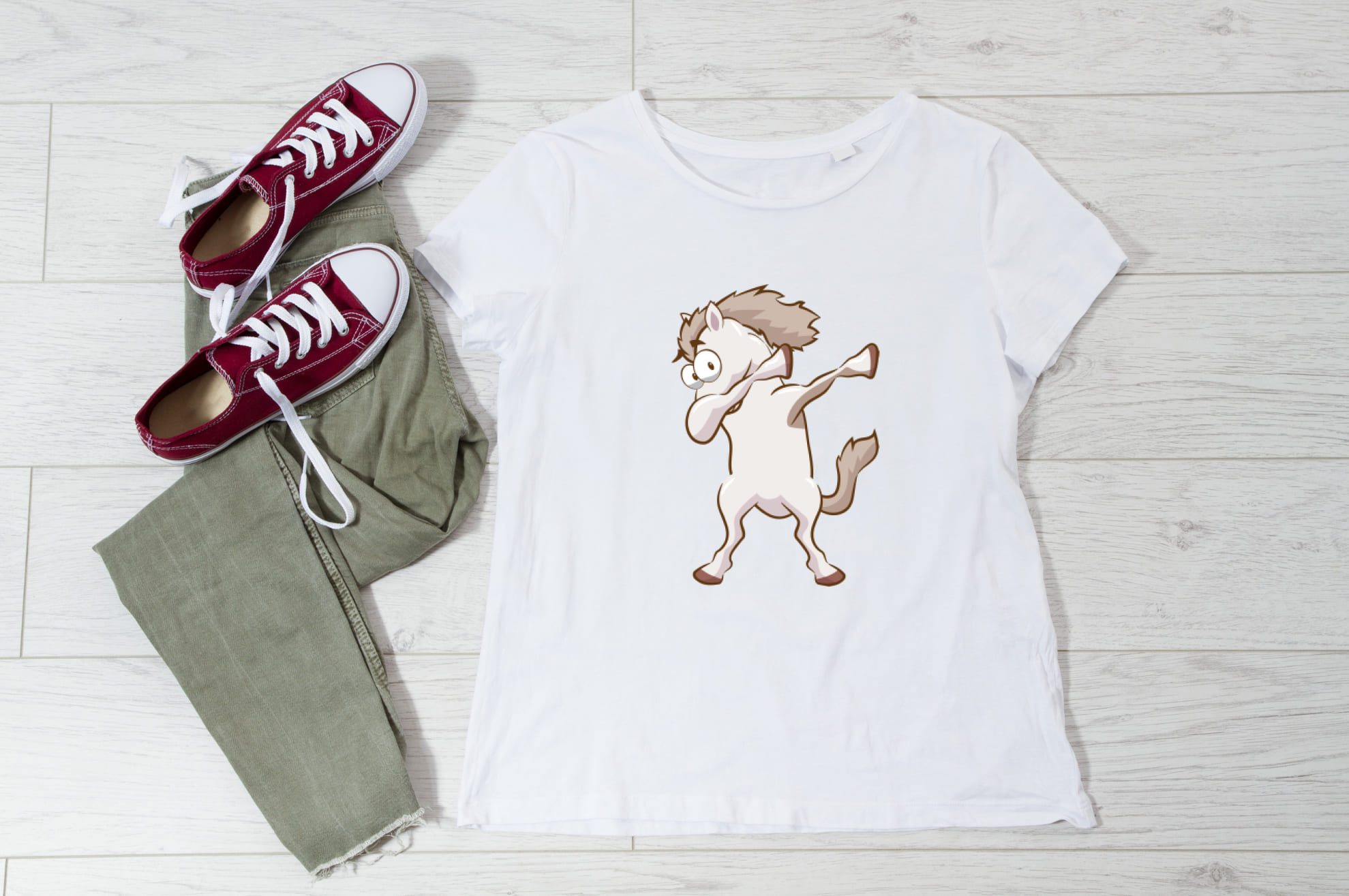 White t-shirt with an image of a milk baby horse, and sneakers with trousers on the wooden background.