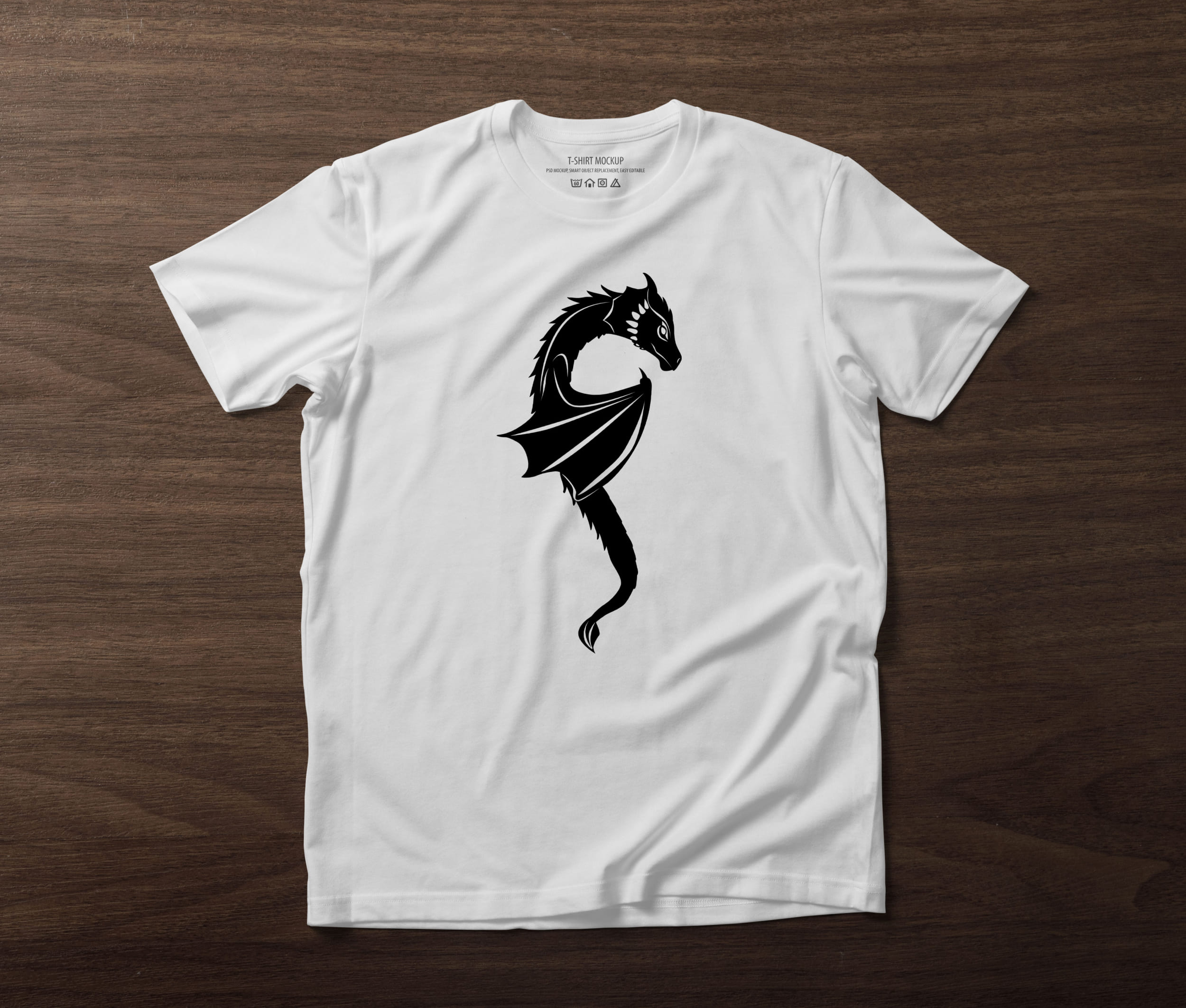 A white t-shirt on a table with a black silhouette of a little dragon.