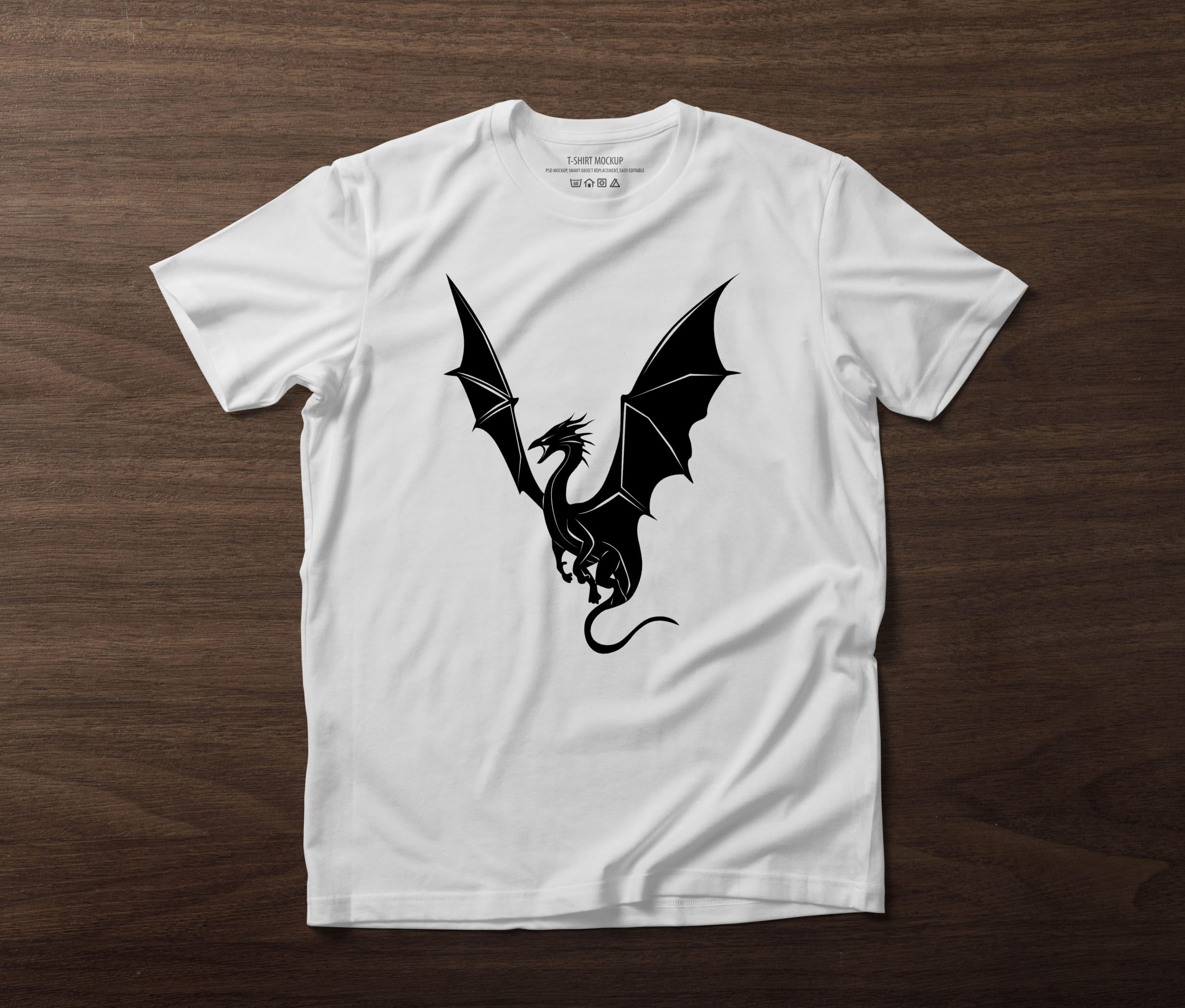 A white t-shirt on a table with a black silhouette of a dragon.