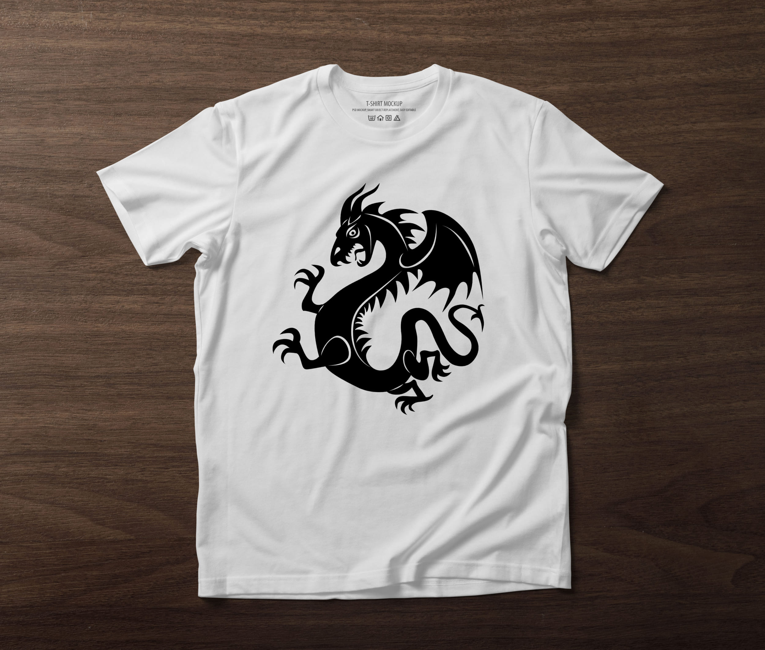A white t-shirt on a table with a black silhouette of a dragon.