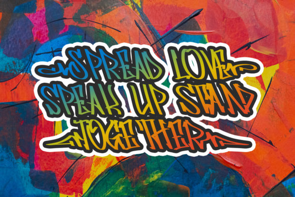 Green, yellow, orange and blue gradient "Spread love speak up stand together" lettering in graffiti font on a graffiti background.