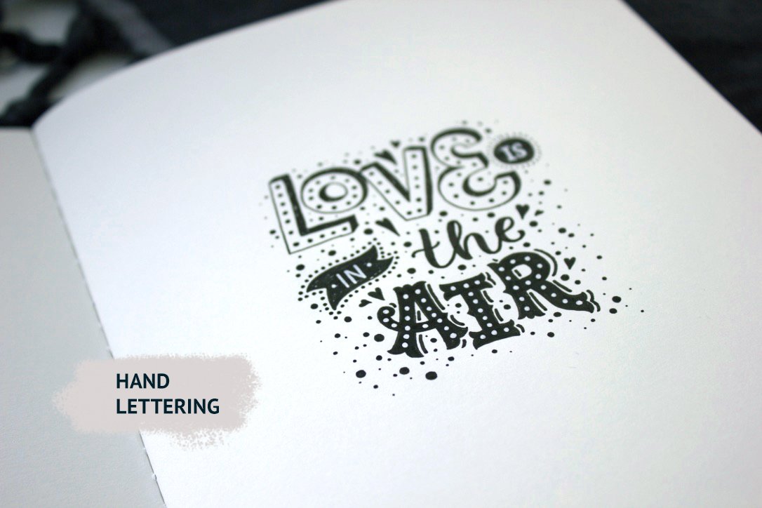 Hand black lettering "Love in the air" on a white sheet.
