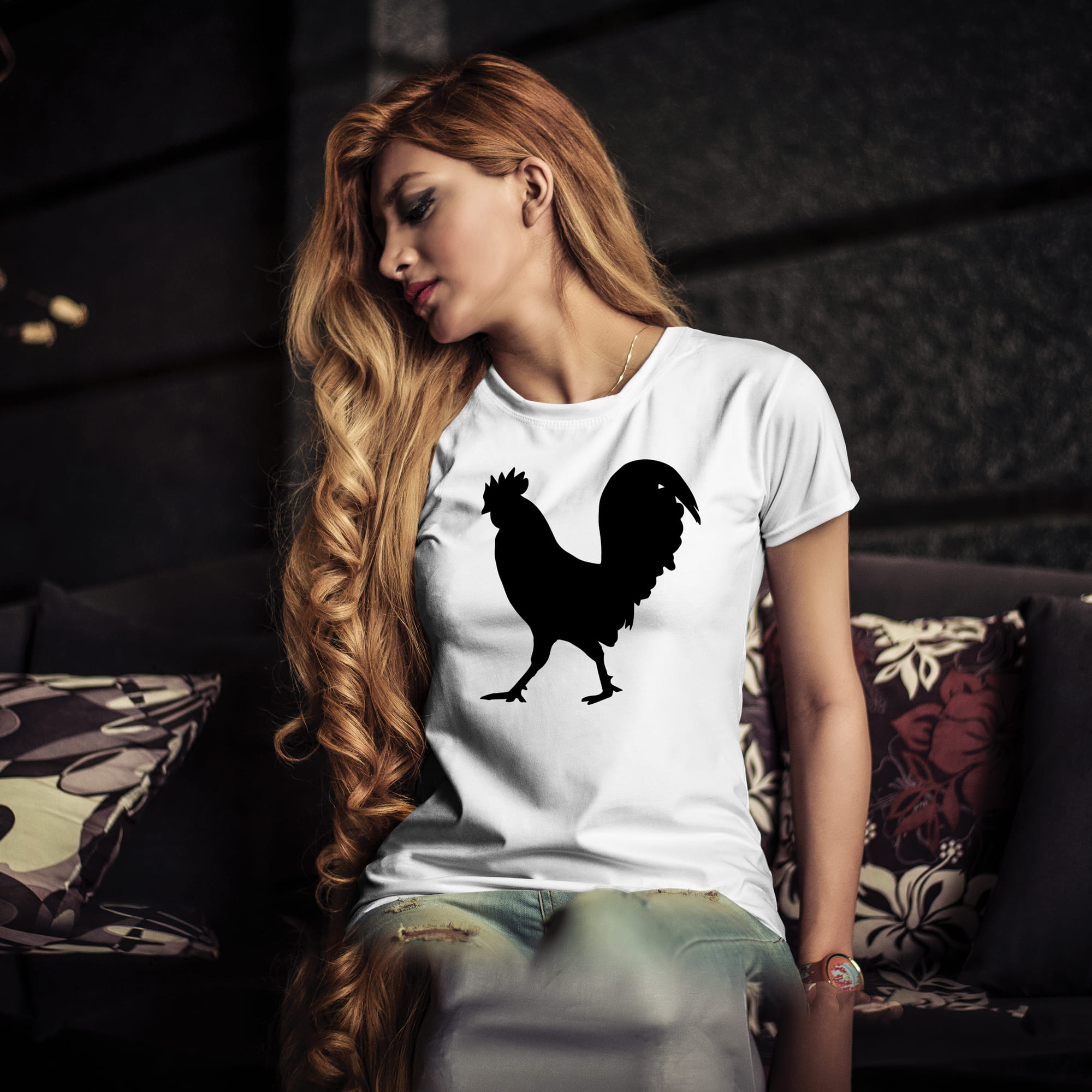 Woman sitting on a couch wearing a t - shirt with a rooster on it.