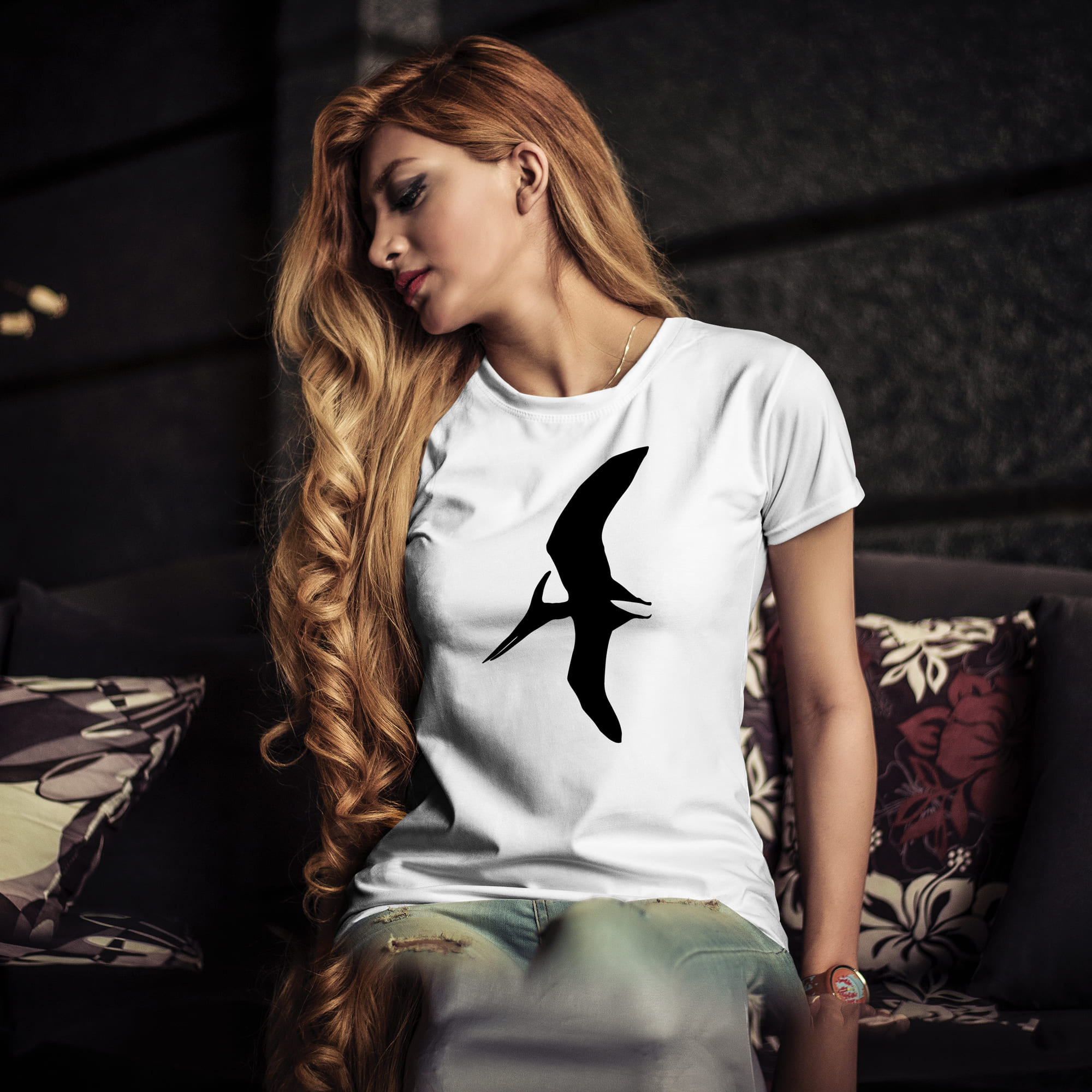 Woman sitting on a couch wearing a t - shirt with a bird on it.