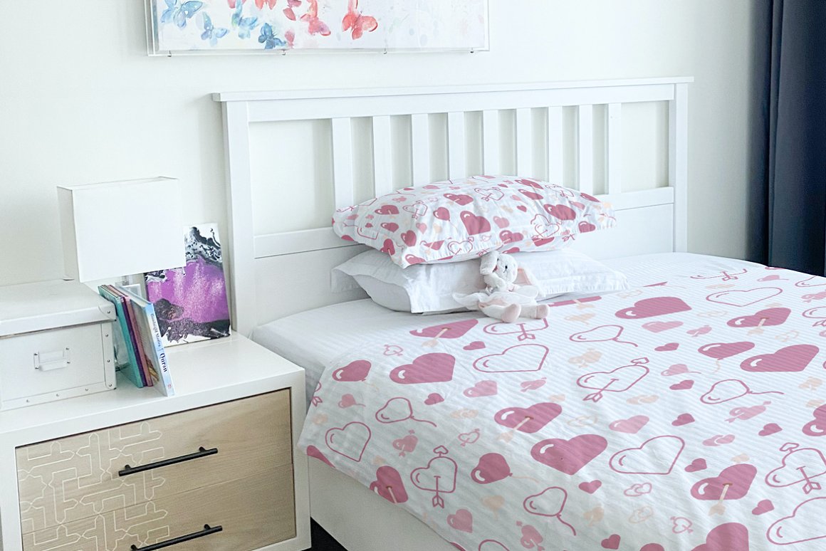 A white bedclothes with pink different hearts on a white bed.