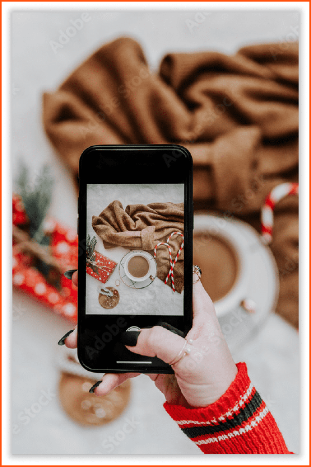 A woman is holding a phone and taking a picture of coffee, a gift, candies, and a blanket.