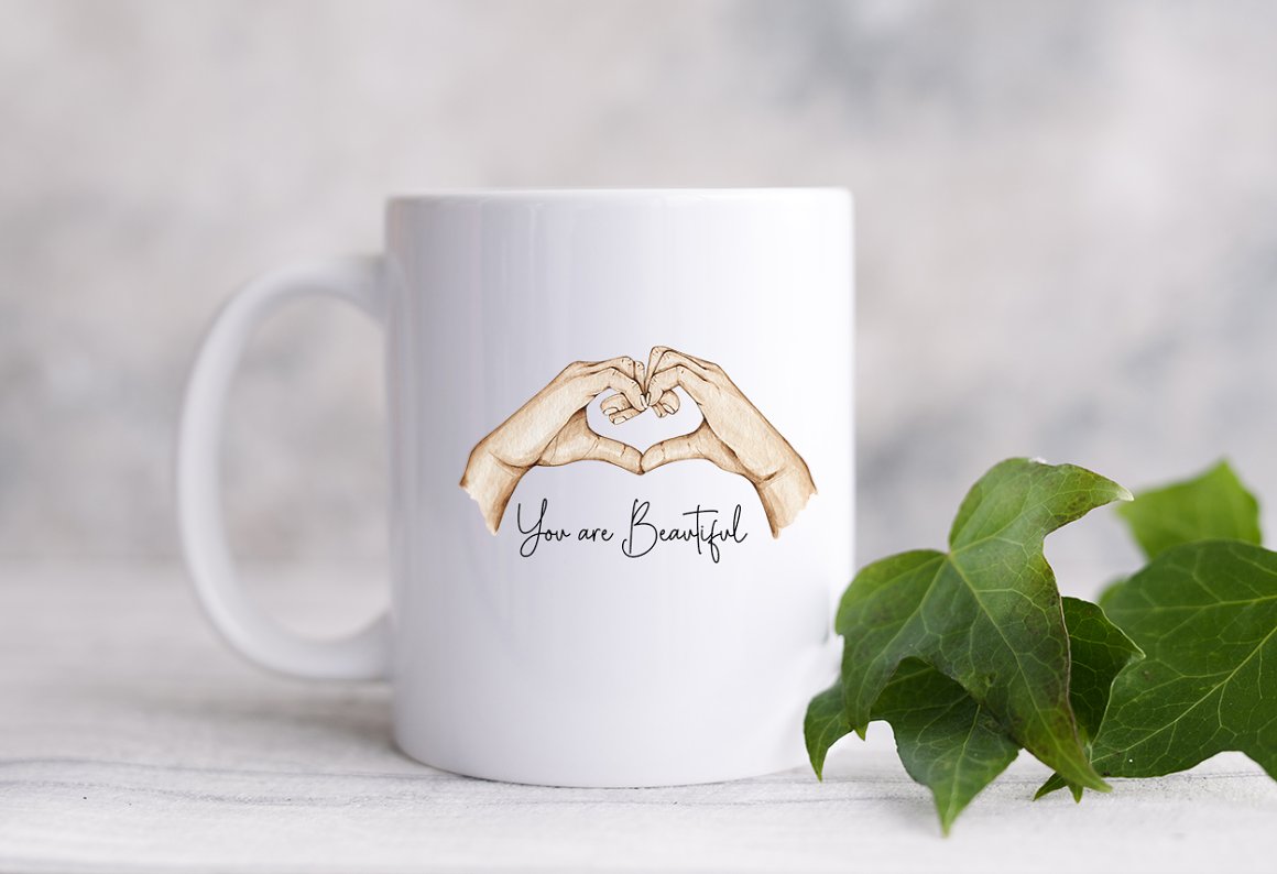 White cup with black lettering "You are beautiful" and illustration of heart mother.