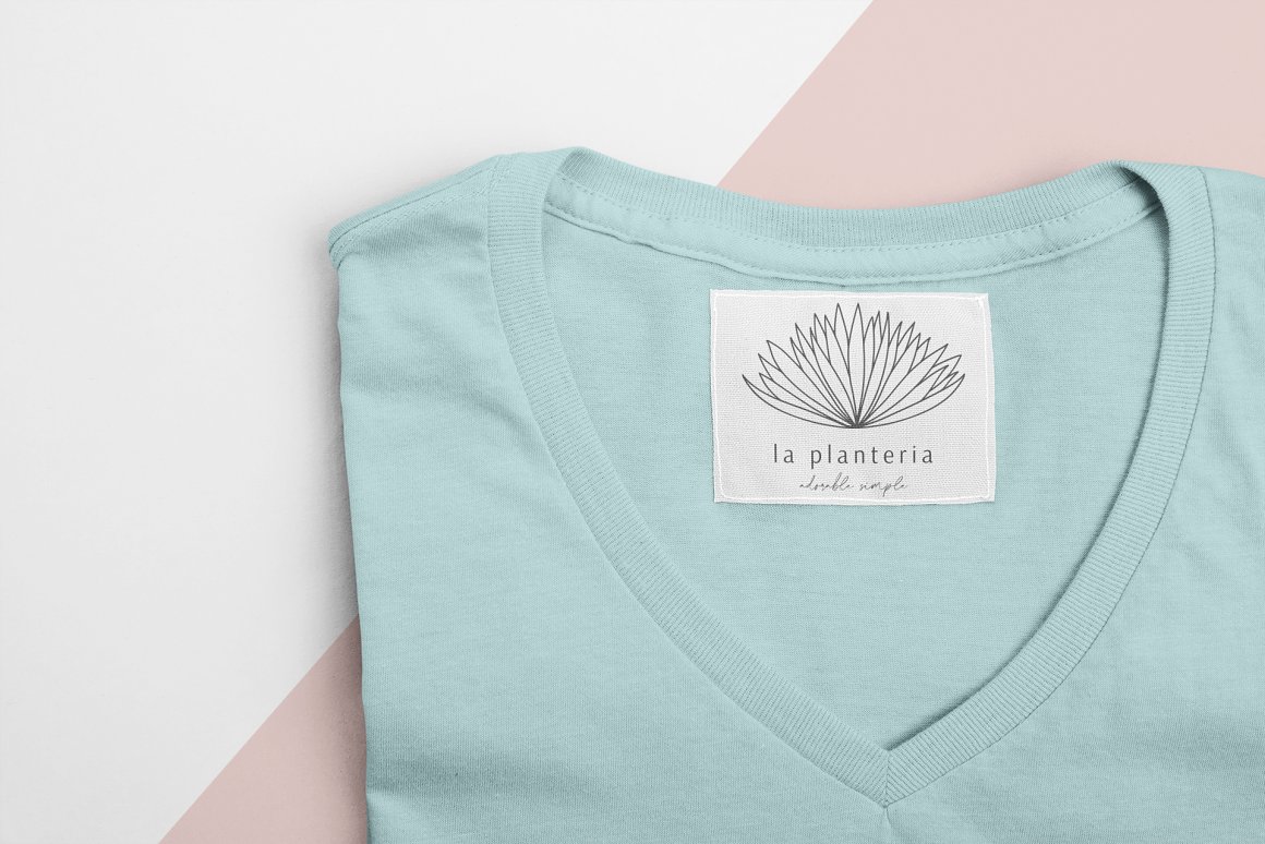 Light blue t-shirt with white label with black logo "la planteria" on a gray-pink background.
